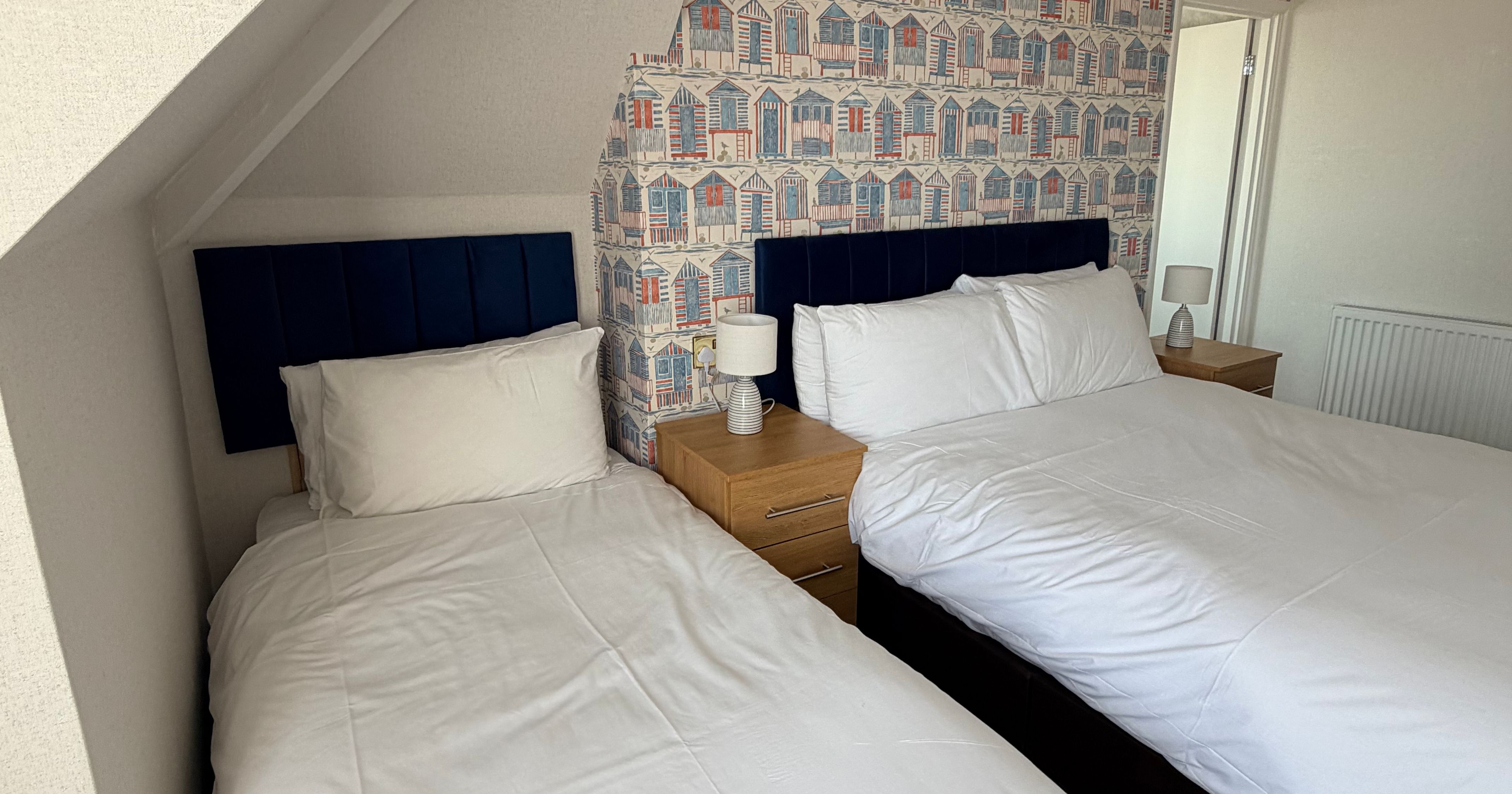 Twin bedroom with two single beds, navy headboards and seaside hut wallpaper