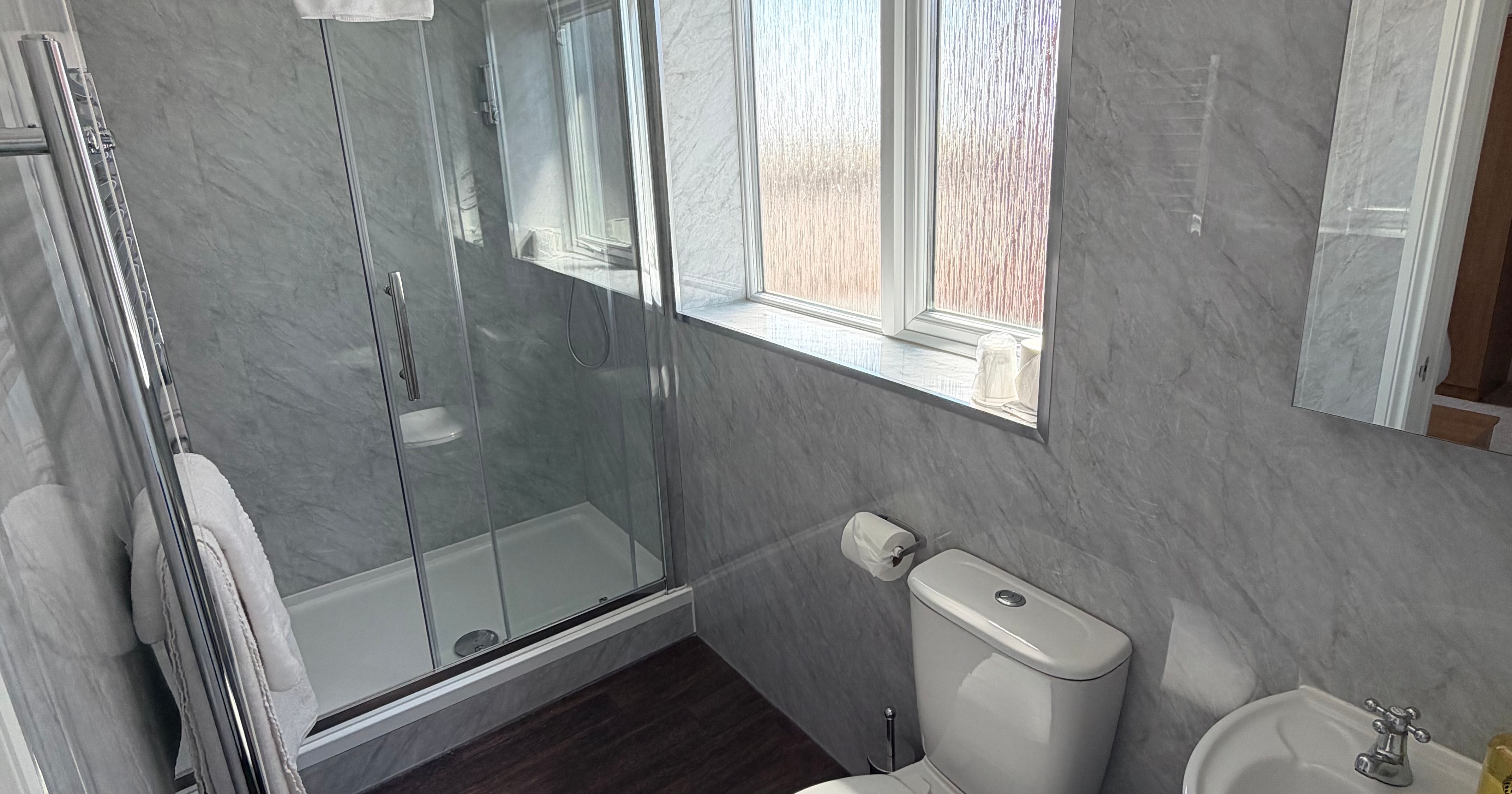 Modern lodge bathroom with glass shower enclosure, toilet and hand basin beside frosted window