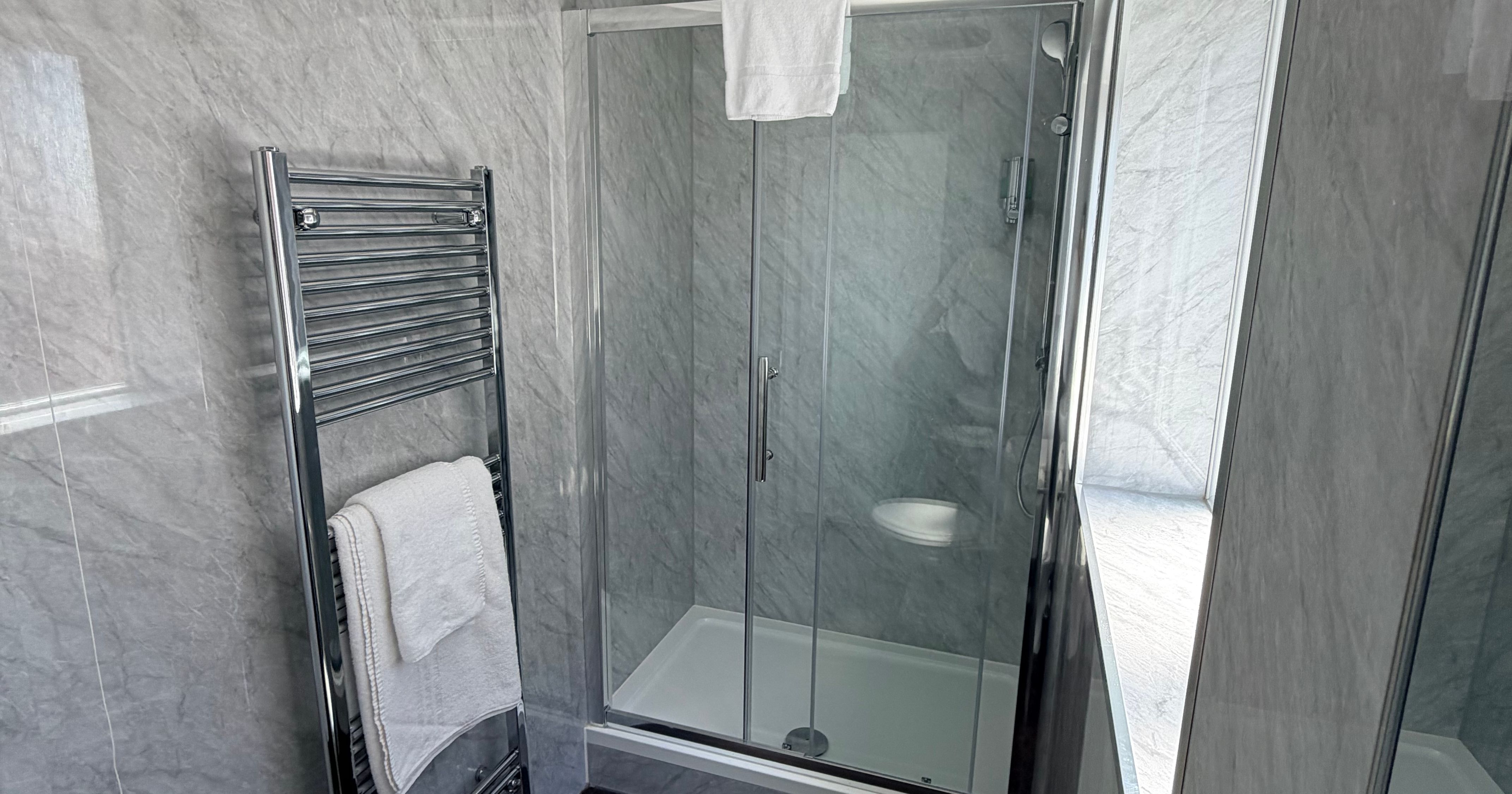 Modern lodge bathroom with glass shower enclosure, chrome heated towel rail and grey tiled walls