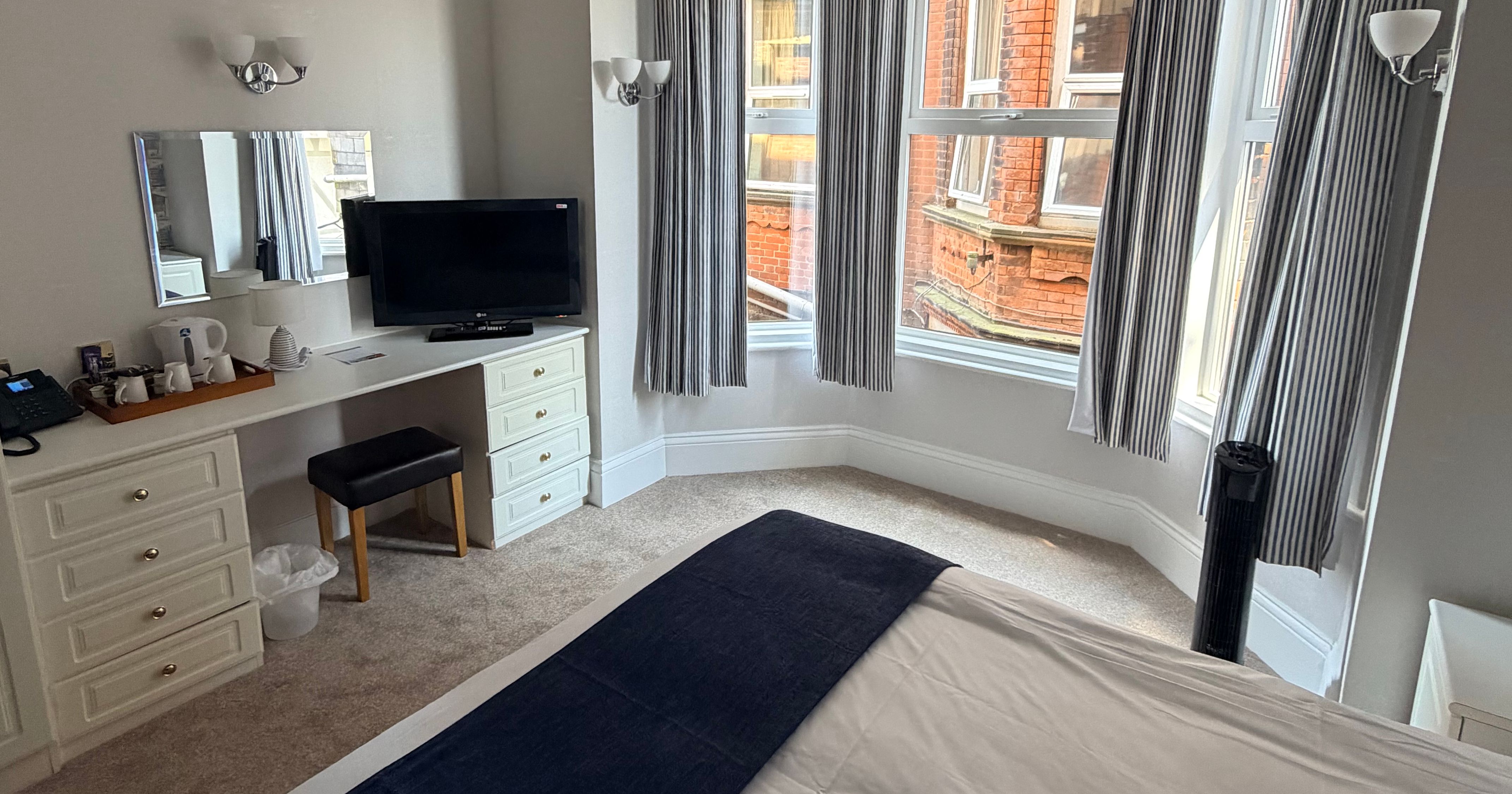 Bright family bedroom with bay windows, striped curtains, desk, TV and neatly made bed