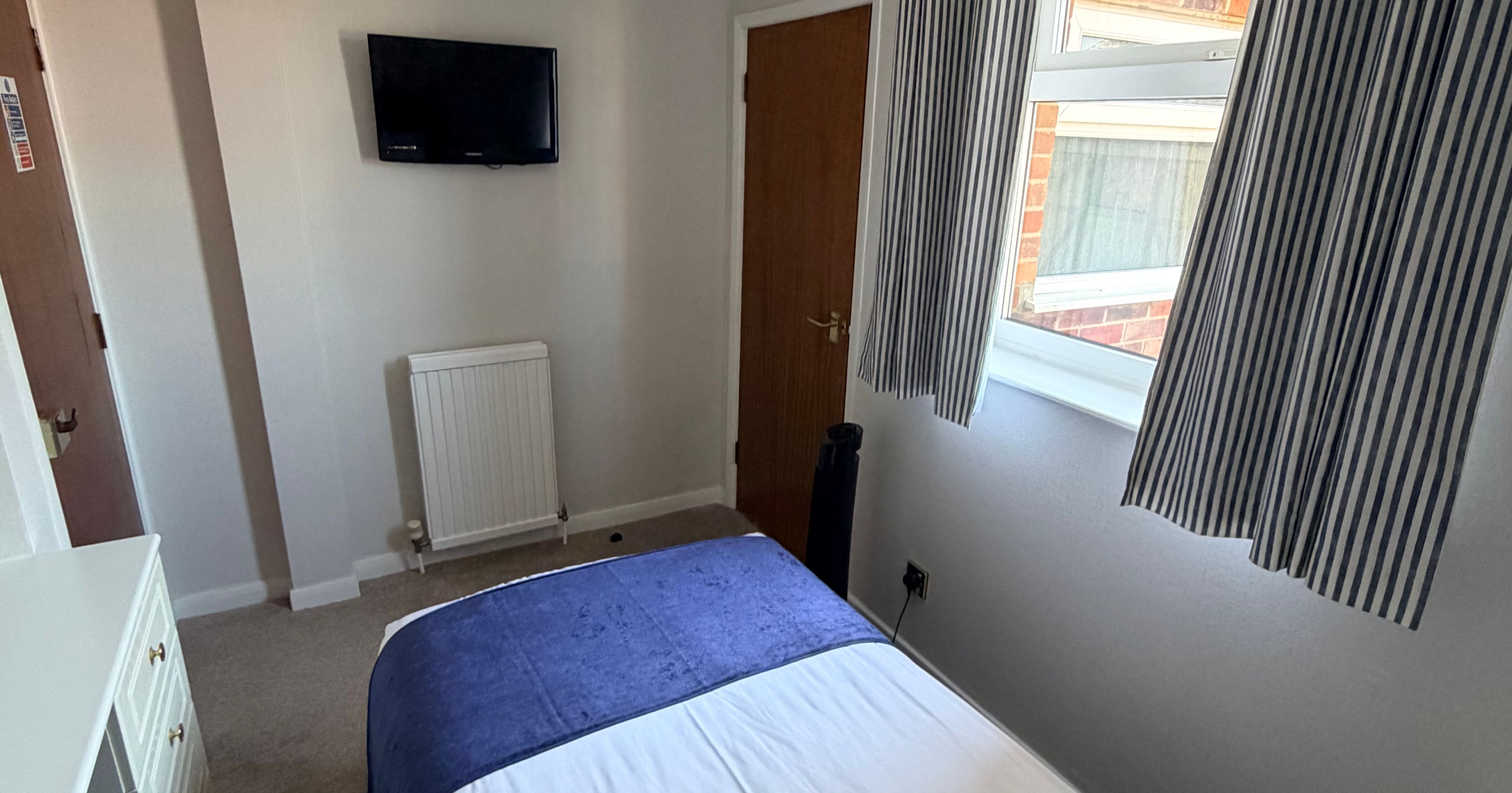 Single bedroom with wall-mounted TV, striped curtains and window