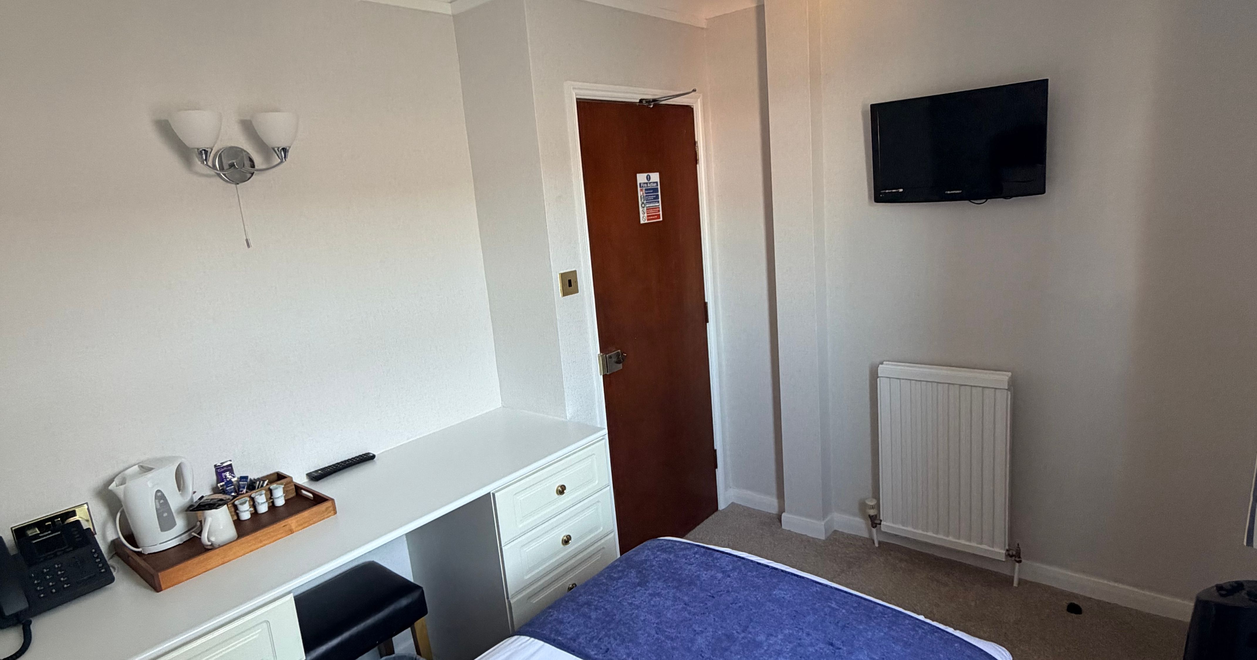 Single hotel room with bed, desk, wall-mounted TV and tea and coffee tray