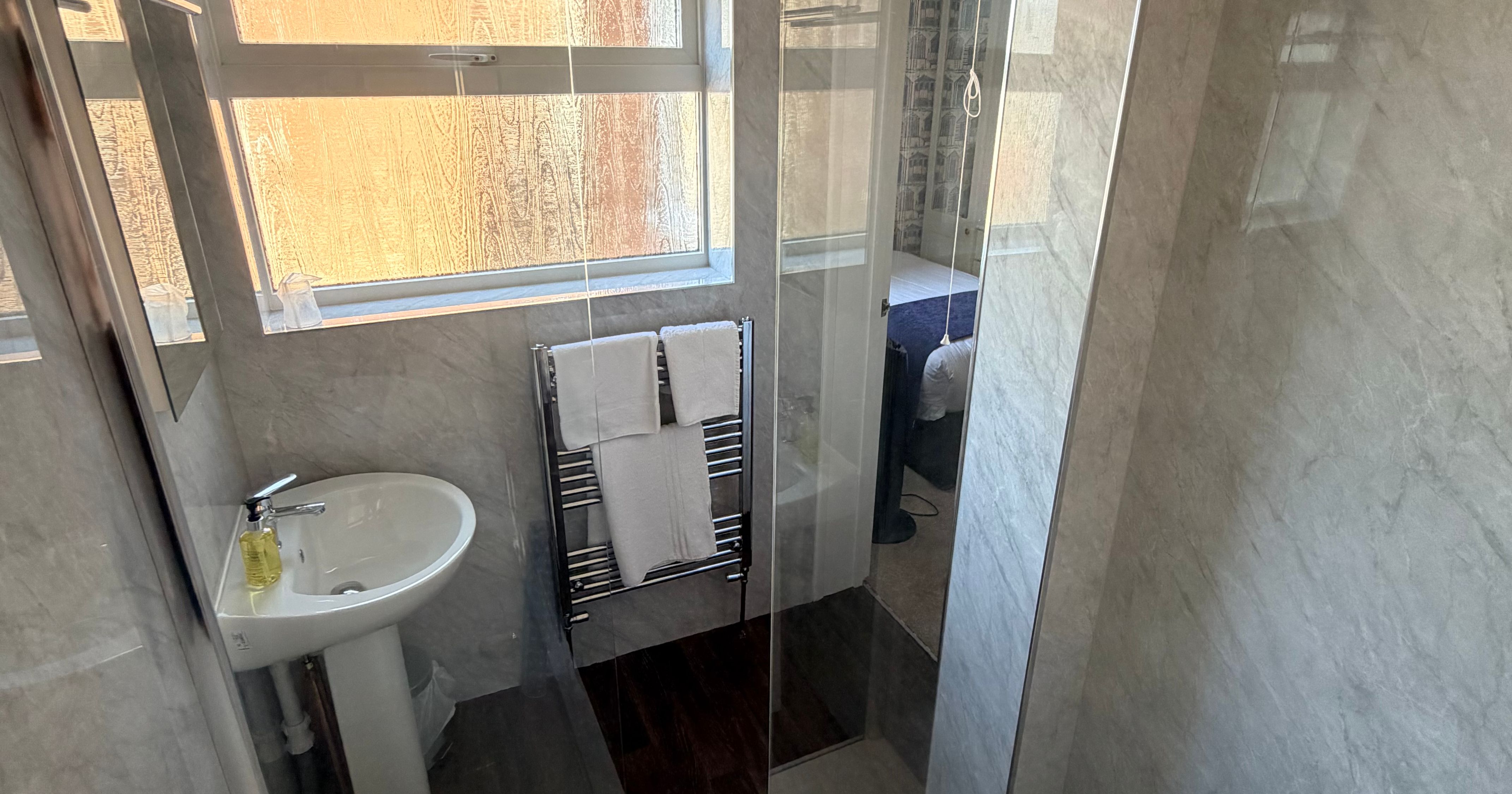 Compact modern bathroom with walk-in shower, pedestal basin, towel radiator and frosted window