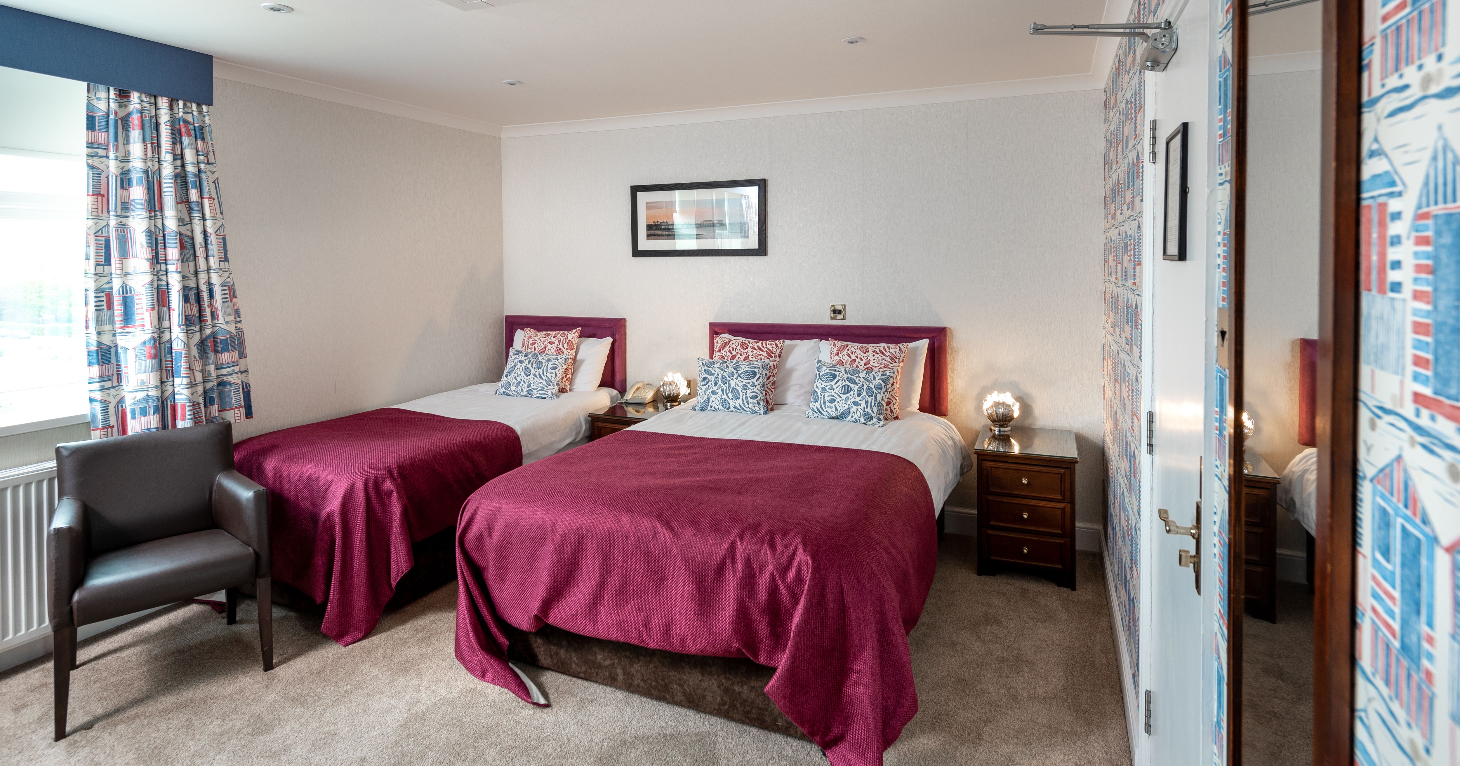 Bright twin bedroom with two beds, burgundy throws, patterned cushions and curtains, and bedside lamps