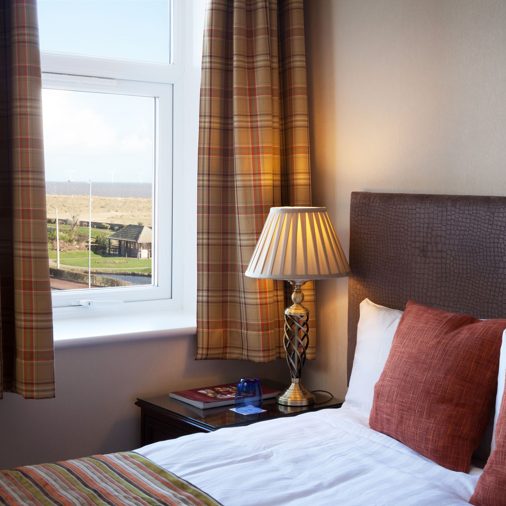 Cosy bedroom with plaid curtains, bedside lamp and sea view through the window