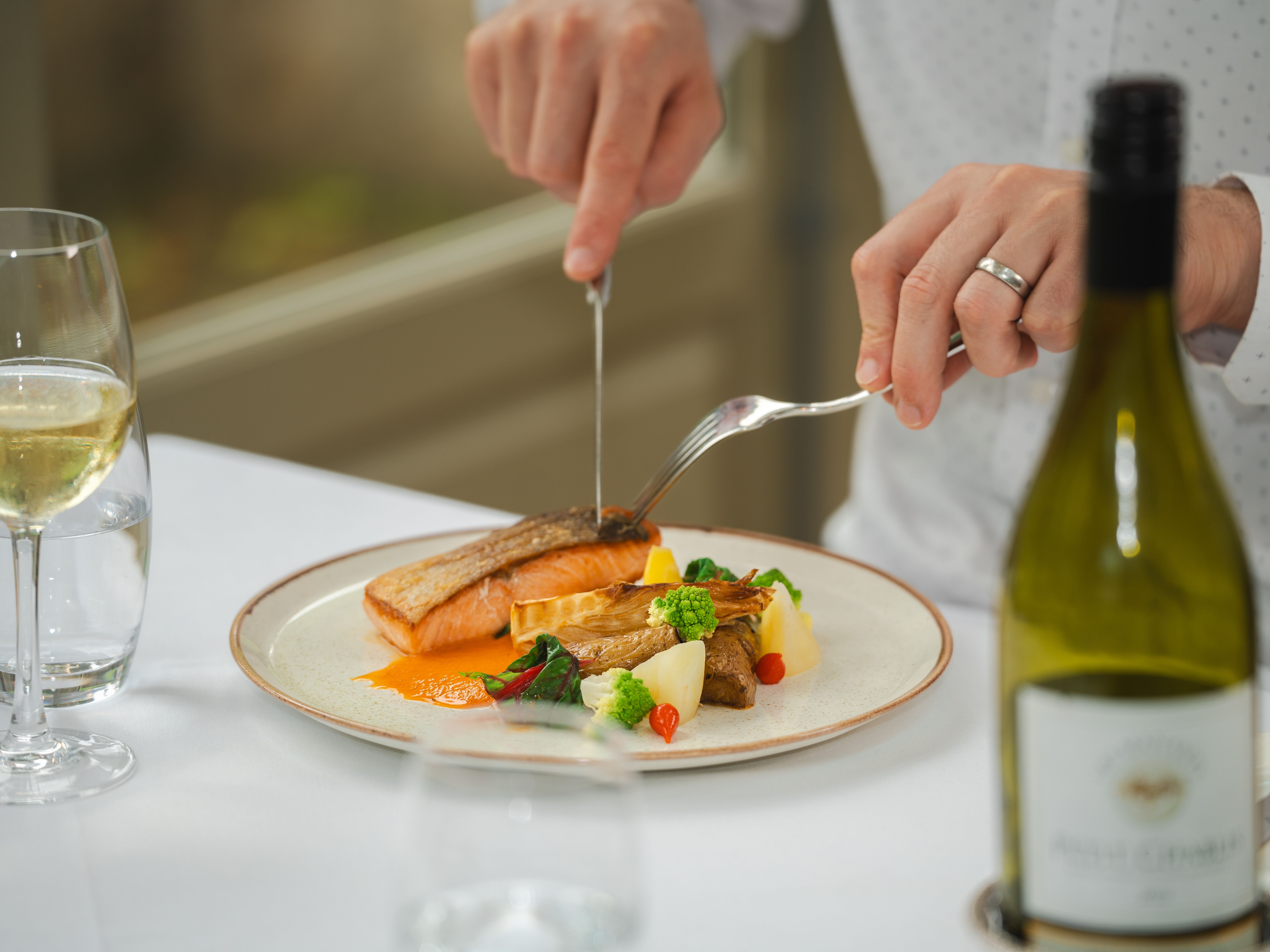 Man cutting into a plate of fish and vegetables