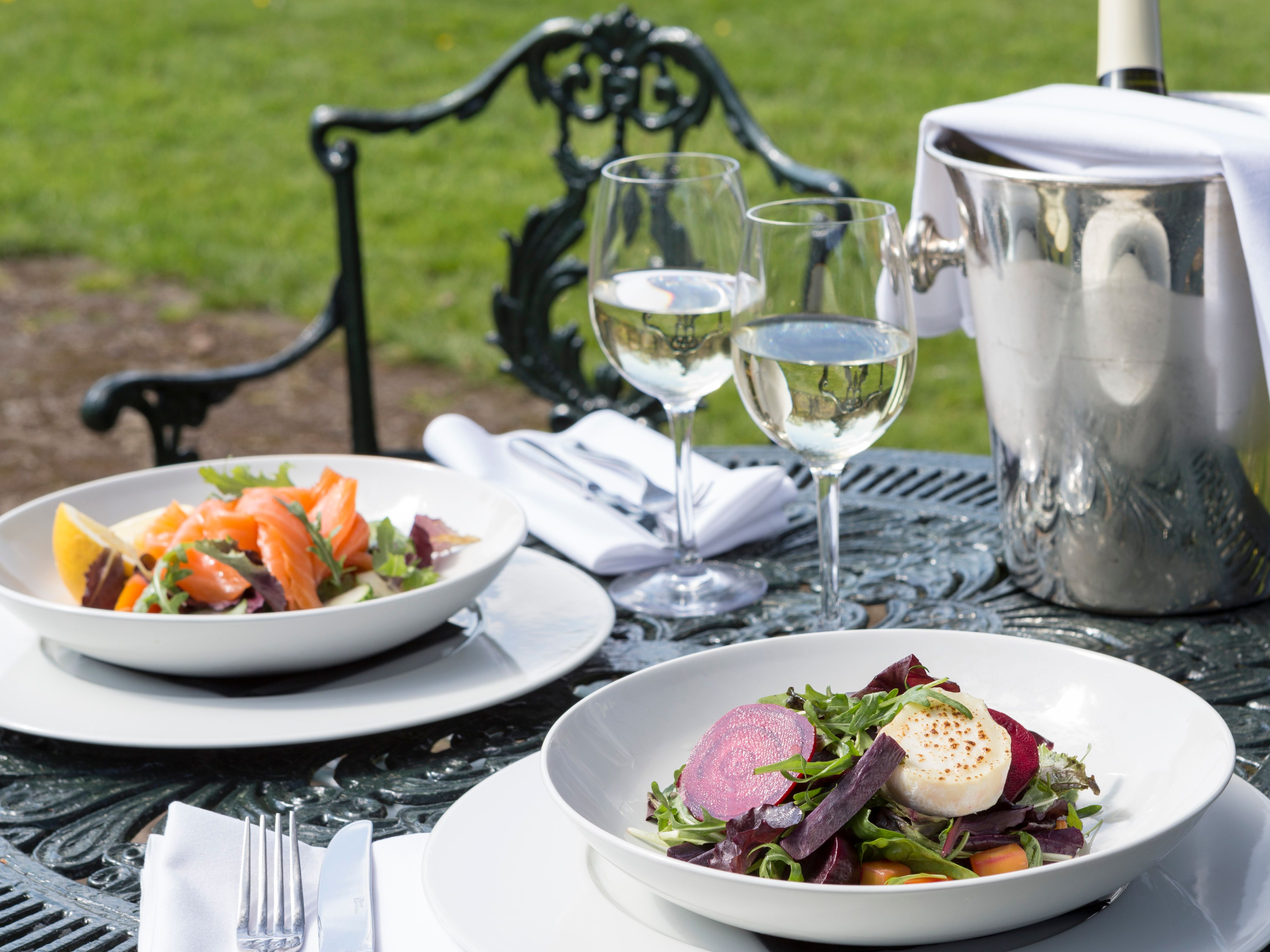 Two plates of food on table next to a cooler of prosecco