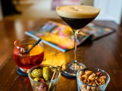 Two cocktails and a bowl of olives set on a table