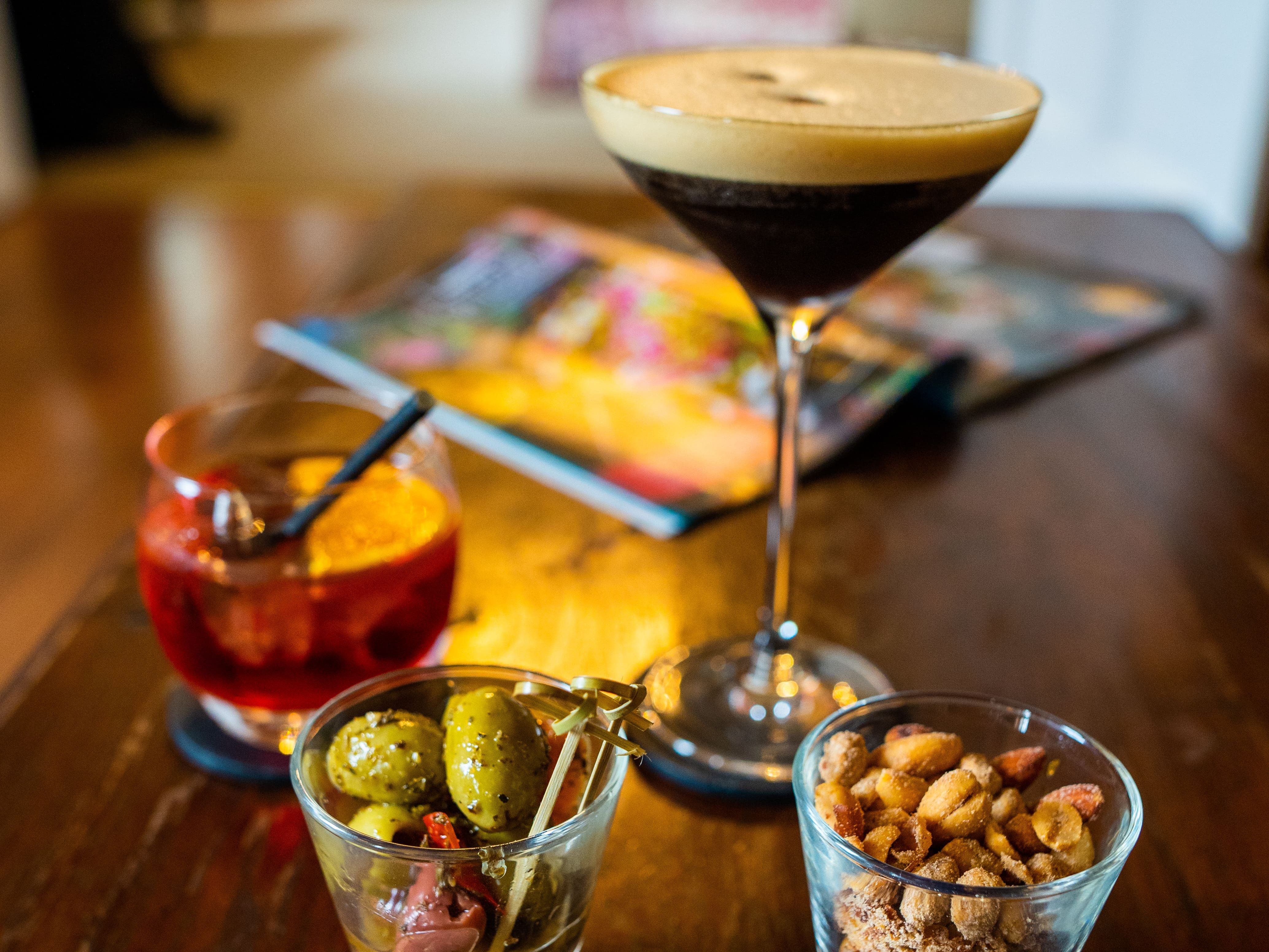Two cocktails and a bowl of olives set on a table