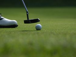Golf ball on grass with club hovering above