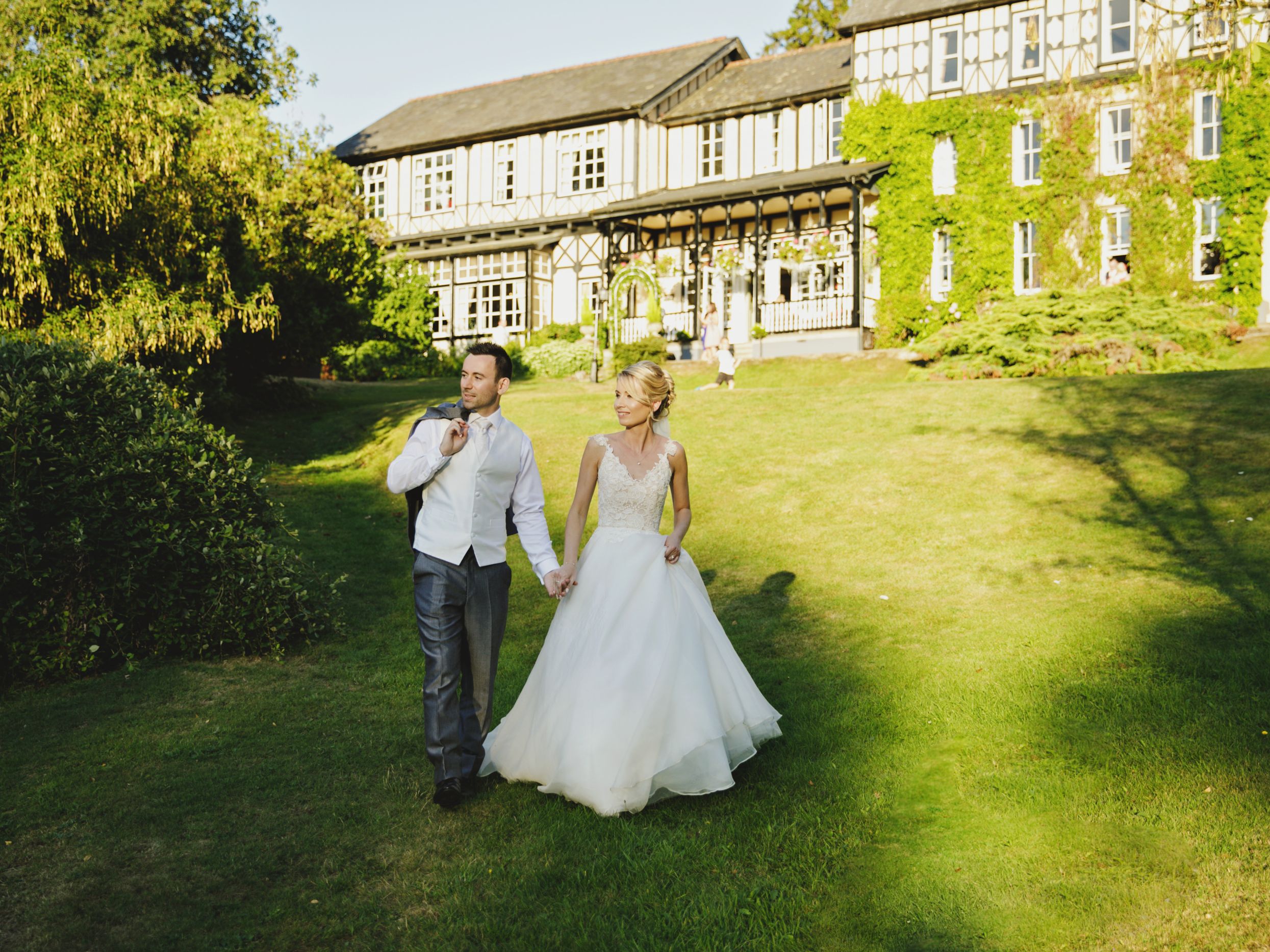 Bride and Groom walking in Grassy Area in front of Lake House