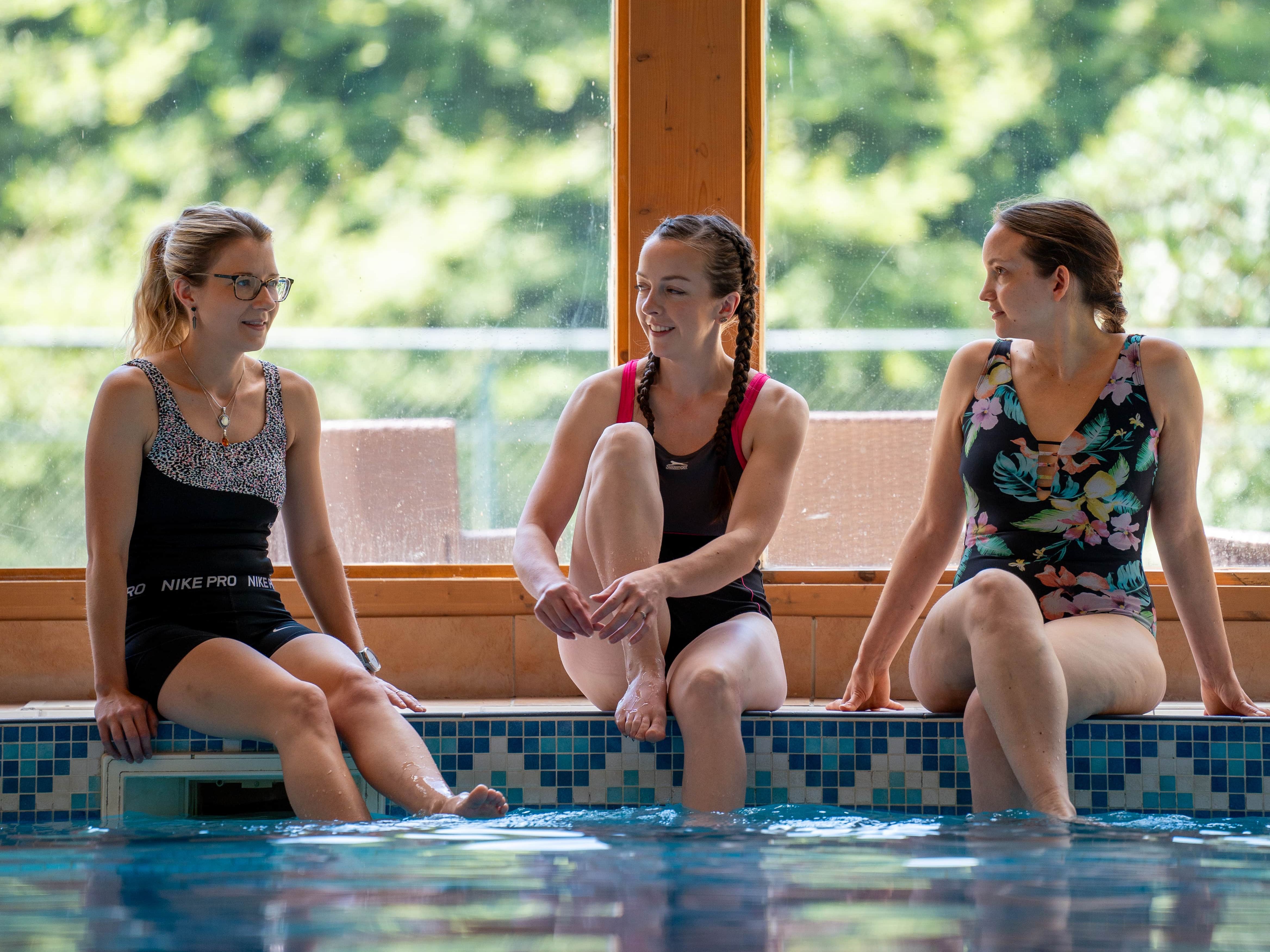 Three poeple enjoying themselves by the pool, with large window in background