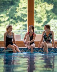 Three poeple enjoying themselves by the pool, with large window in background