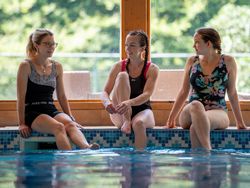 Three poeple enjoying themselves by the pool, with large window in background