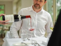Man in white shirt waiting for a glass of red wine to be poured