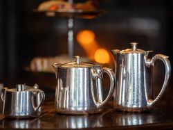 Three silver teapots lined up on a wooden table