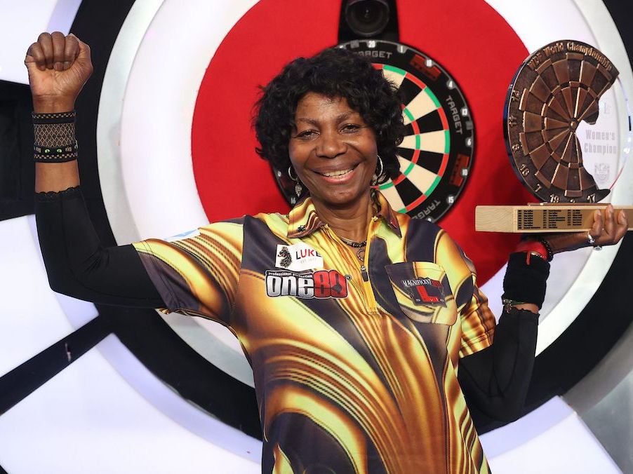 Woman celebrating with a trophy in front of a dartboard