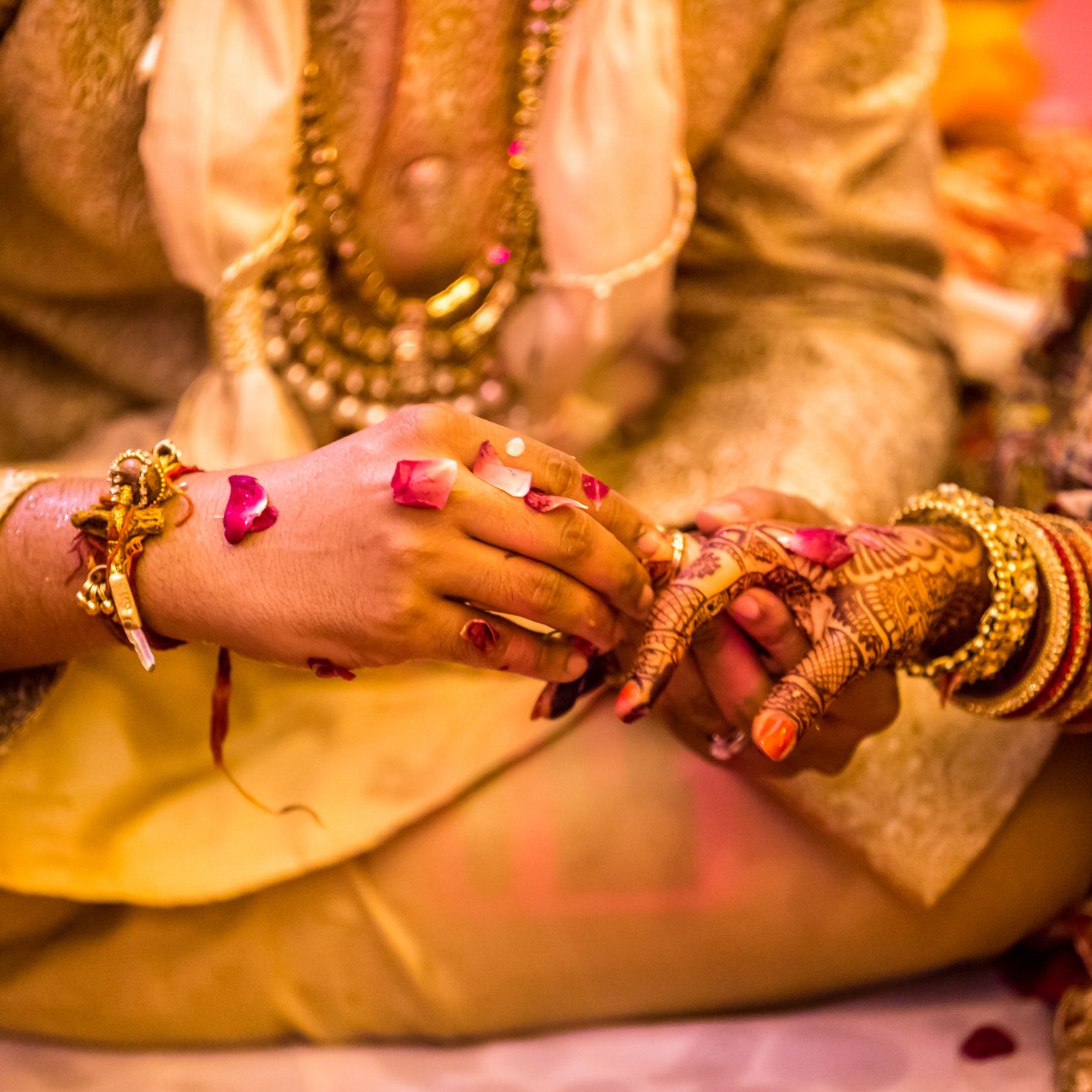 Groom placing a ring on the bride’s henna-decorated hand during a traditional wedding ceremony, with rose petals and ornate jewelry.