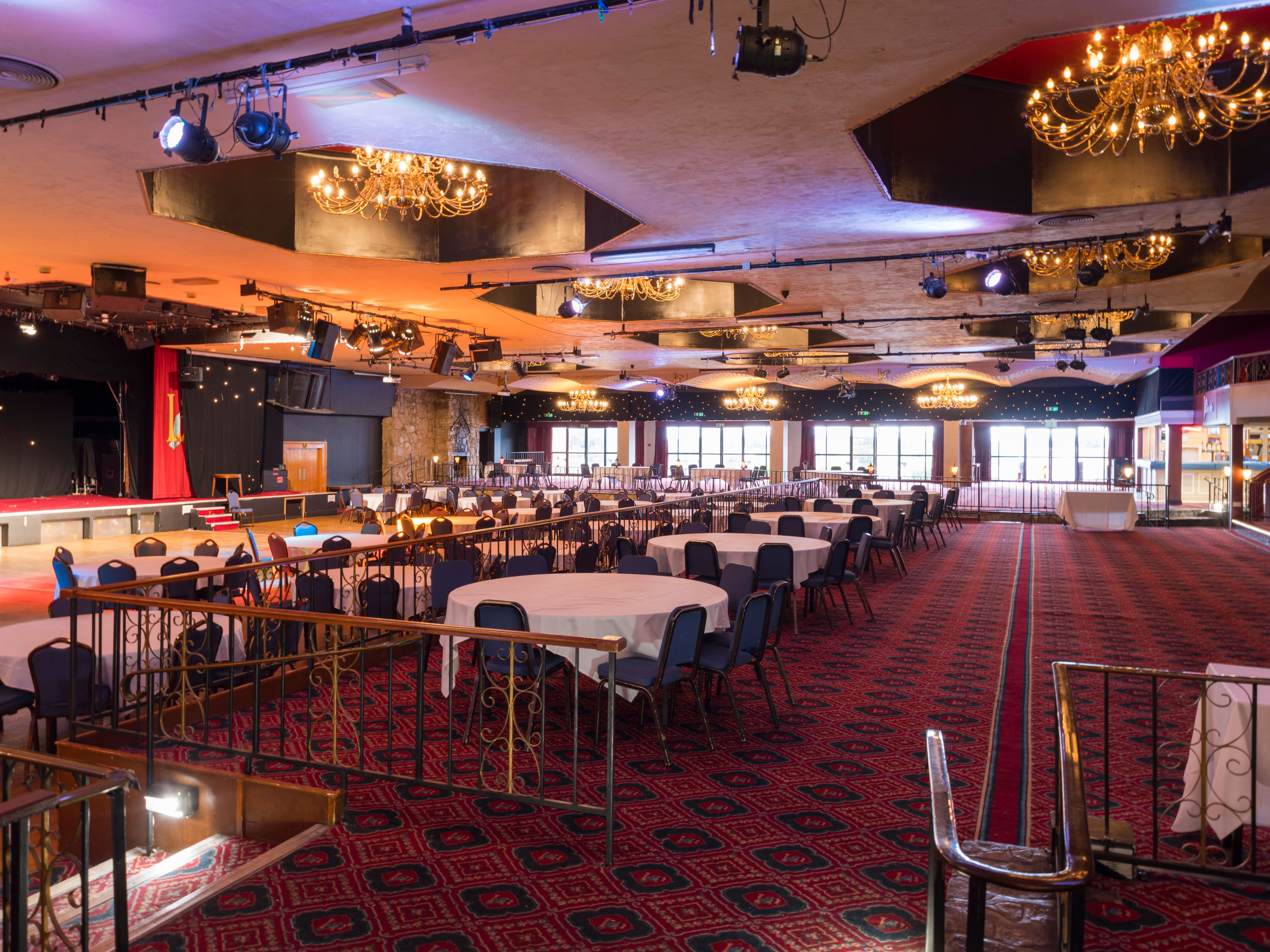 Large banquet hall with chandeliers, round tables, and a stage