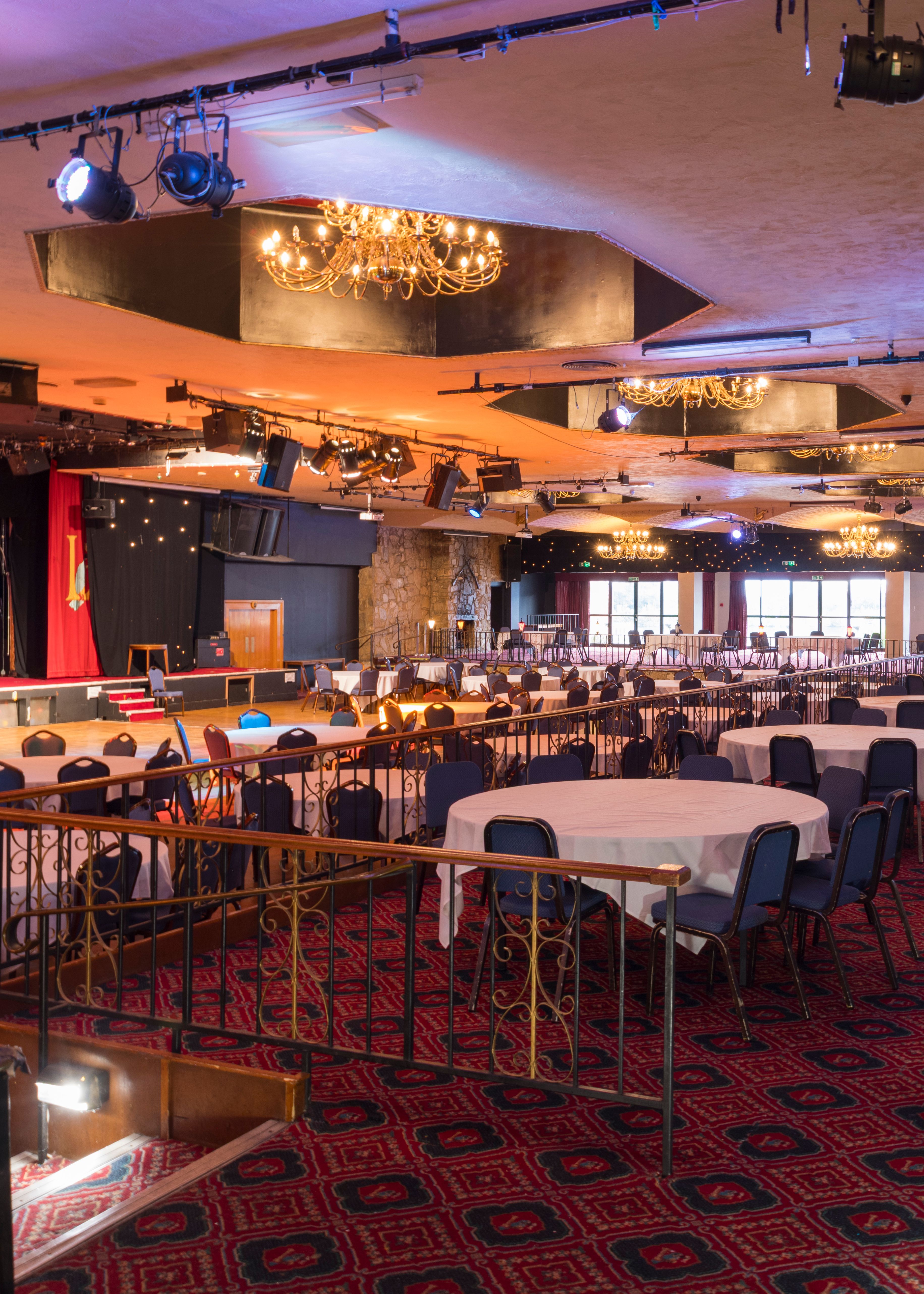 Large banquet hall with chandeliers, round tables, and a stage