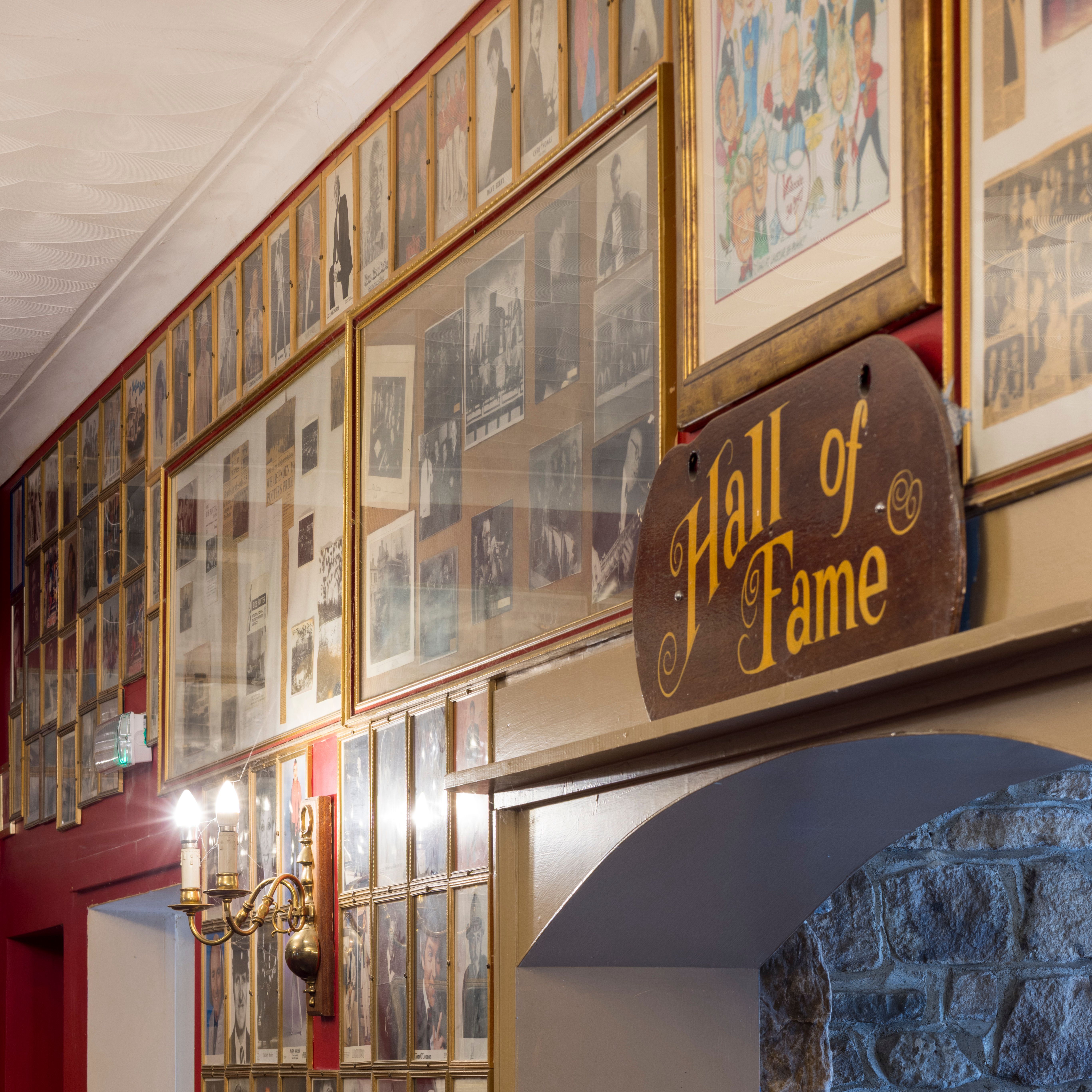 Framed photos and a wooden 'Hall of Fame' sign in a hallway