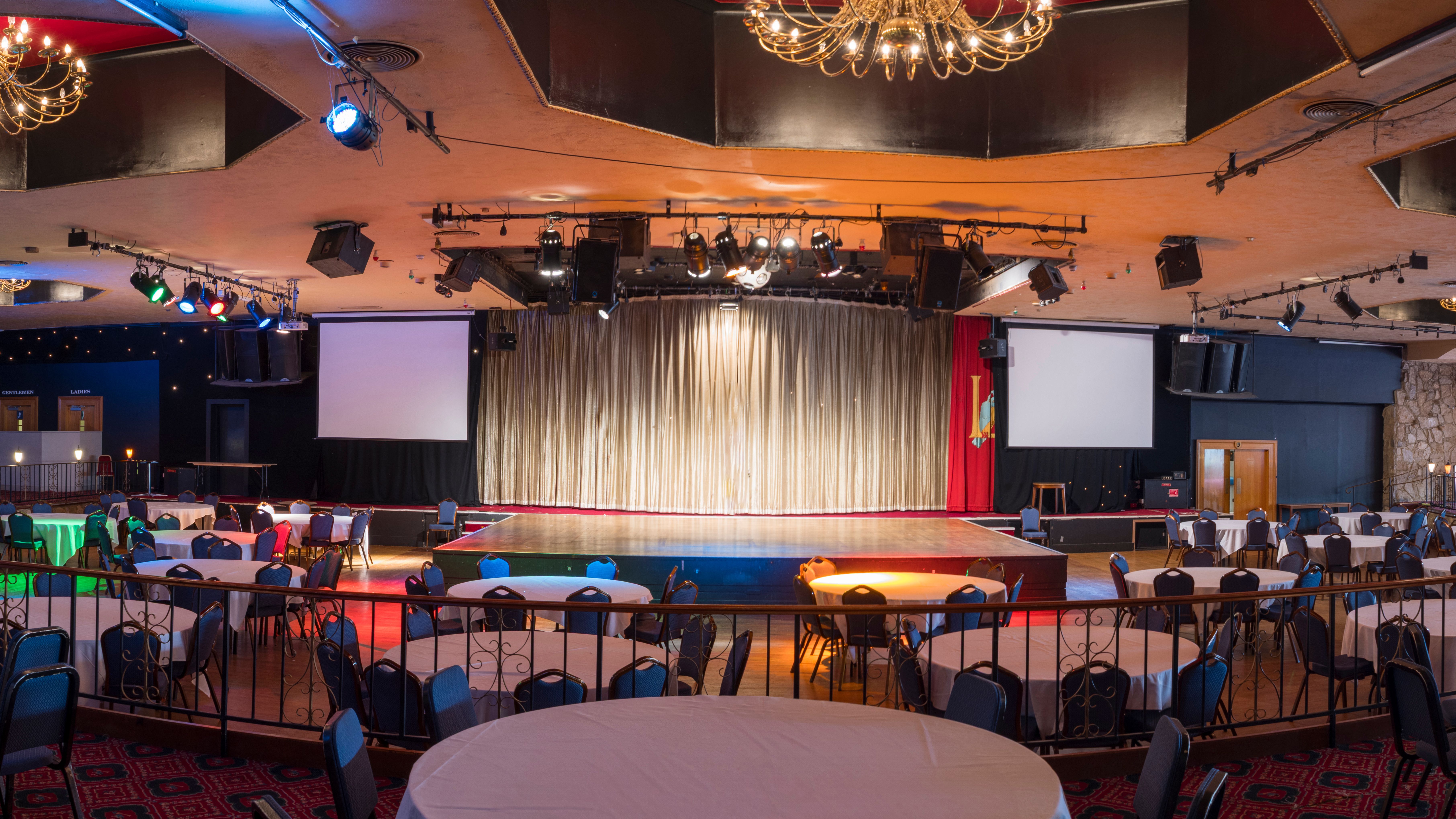 Spacious banquet hall with round tables, stage, and chandeliers