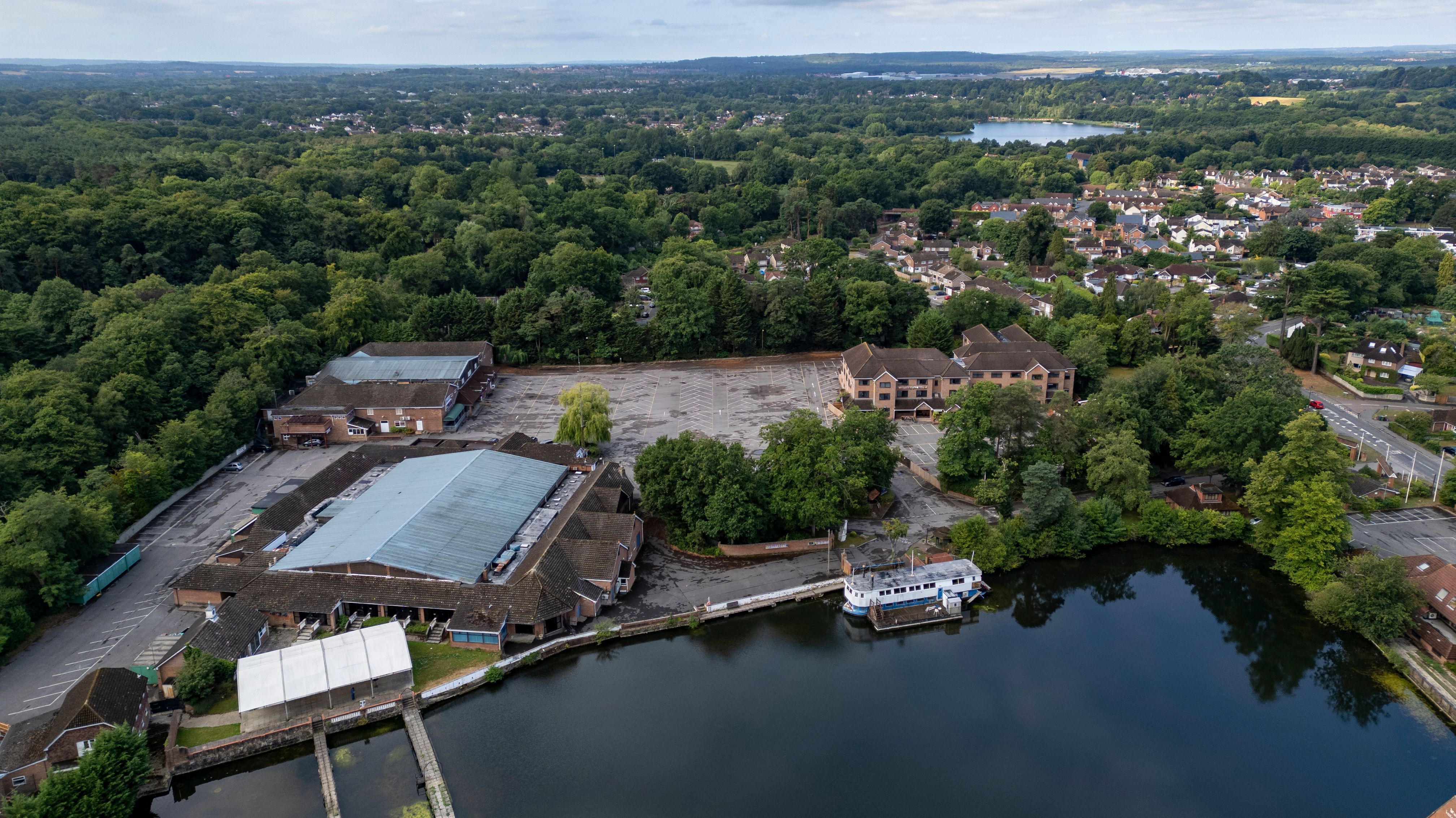 Aerial view of a lakeside building complex surrounded by trees and residential houses.