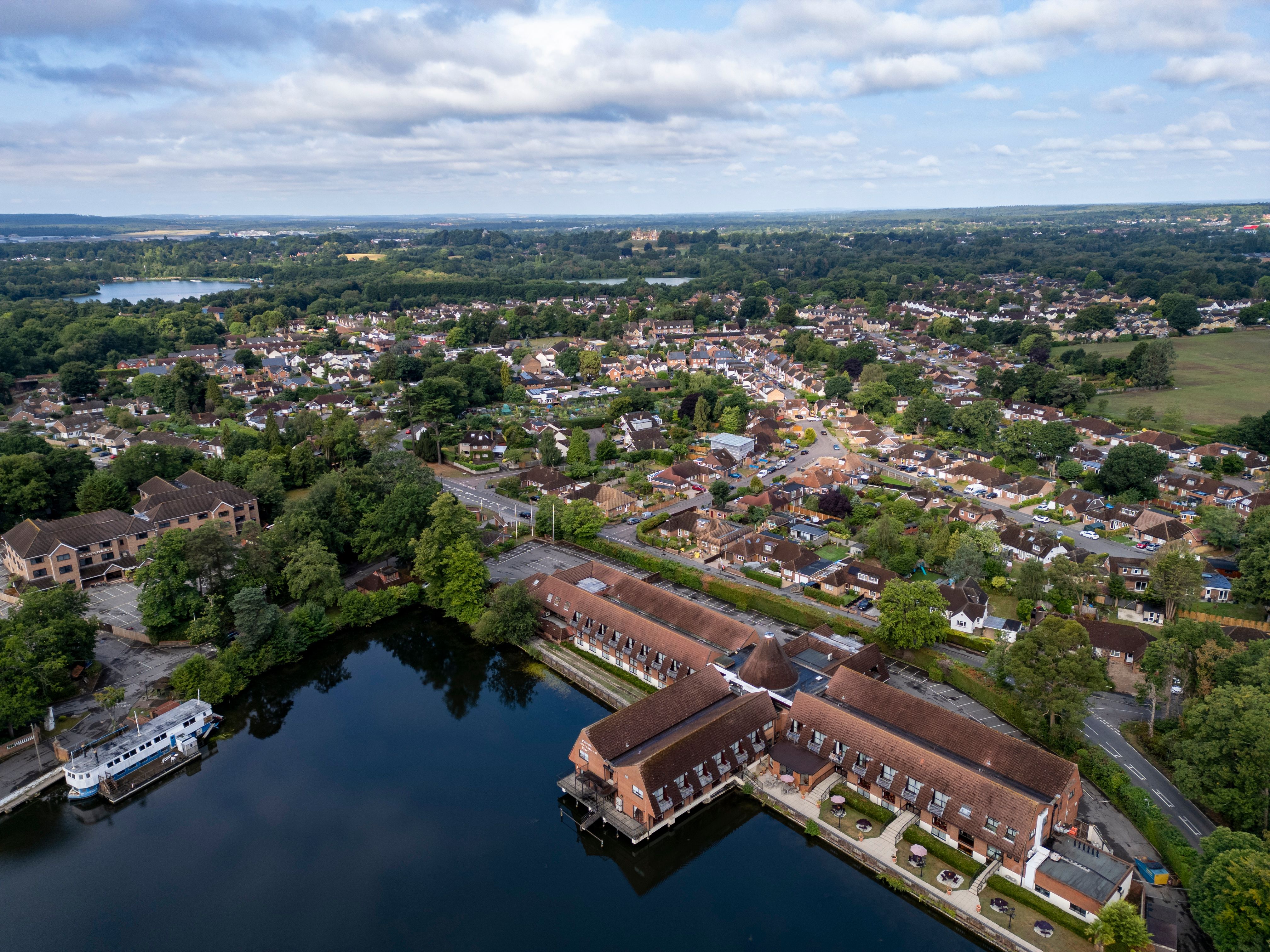 Aerial view of a suburban neighborhood with a lake, houses, and greenery under a partly cloudy sky.