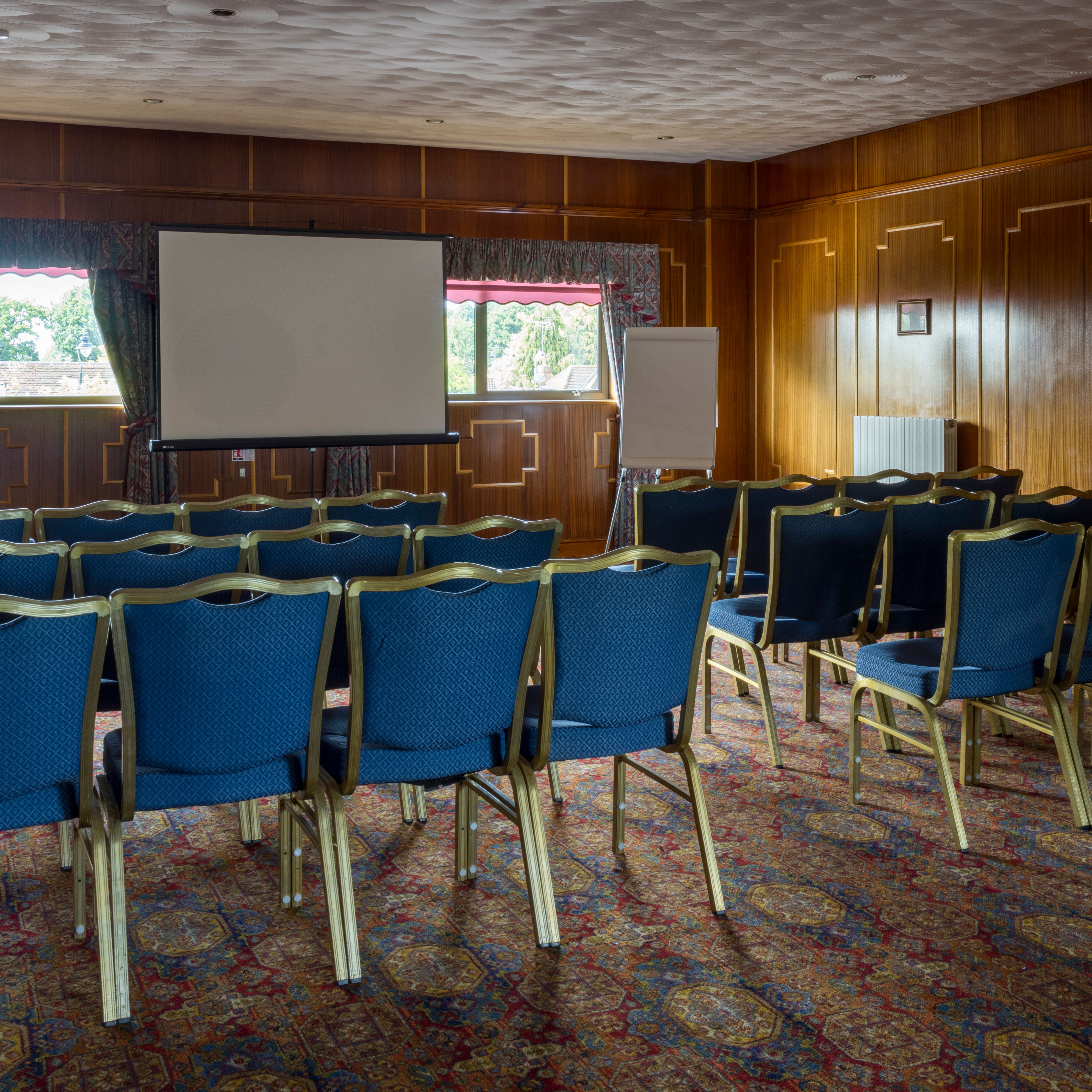 Rows of blue chairs facing a projector screen in a wood-paneled conference room.