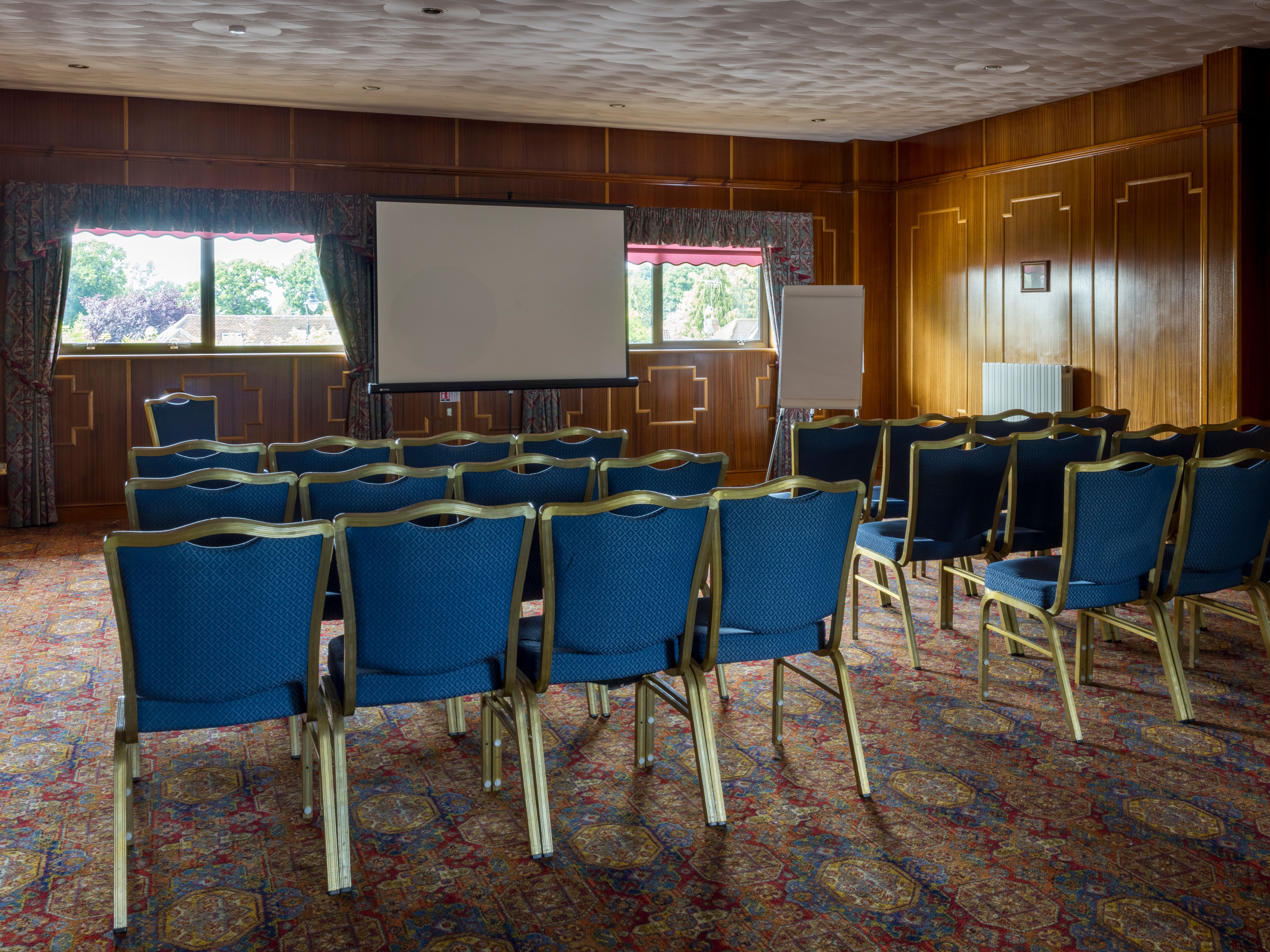 Rows of blue chairs facing a projector screen in a wood-paneled conference room.
