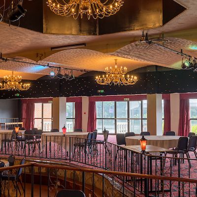 Spacious banquet hall with chandeliers, round tables, and large windows with red curtains