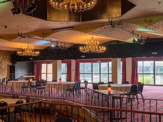 Spacious banquet hall with chandeliers, round tables, and large windows with red curtains