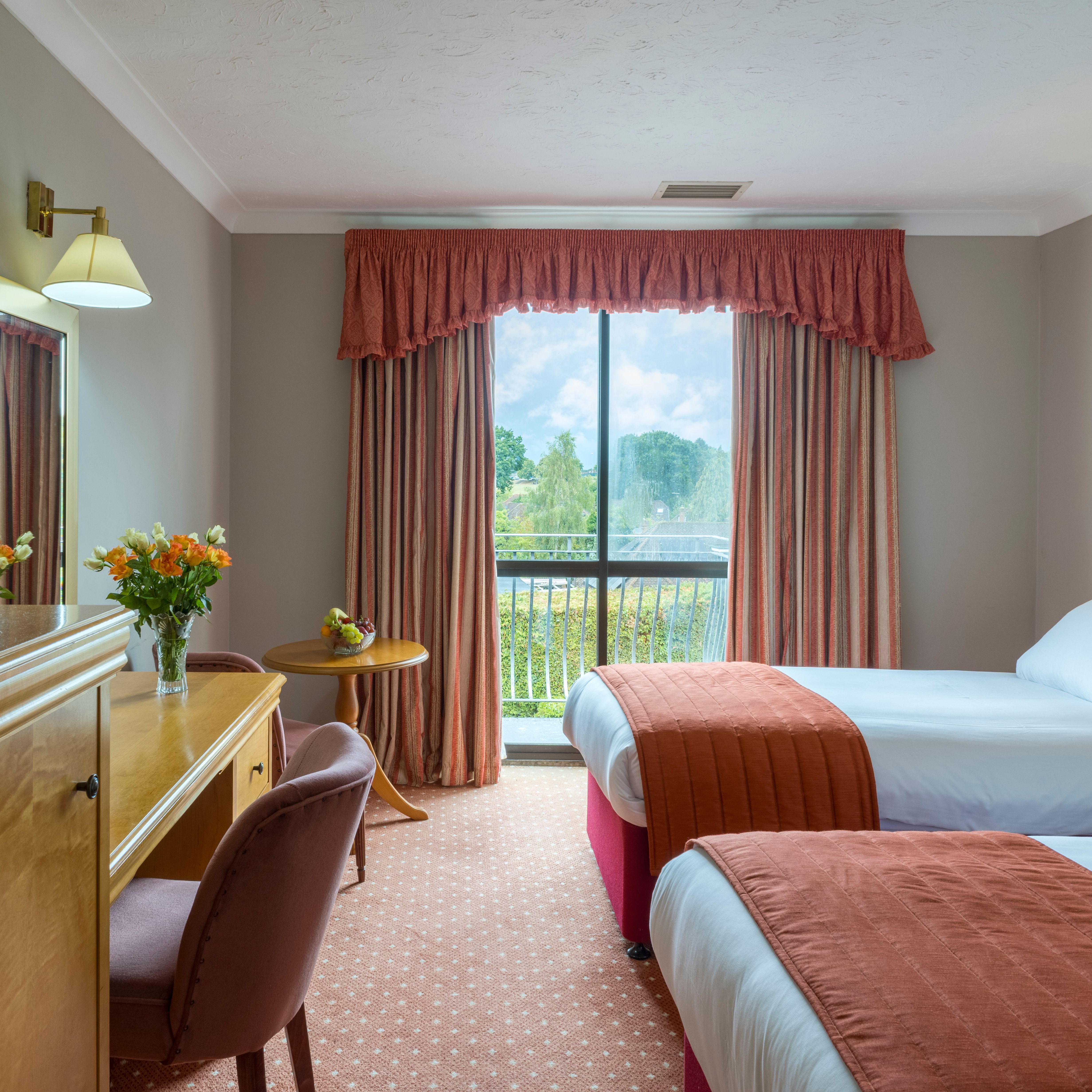 Hotel room with two beds, a large window, and a desk with flowers.