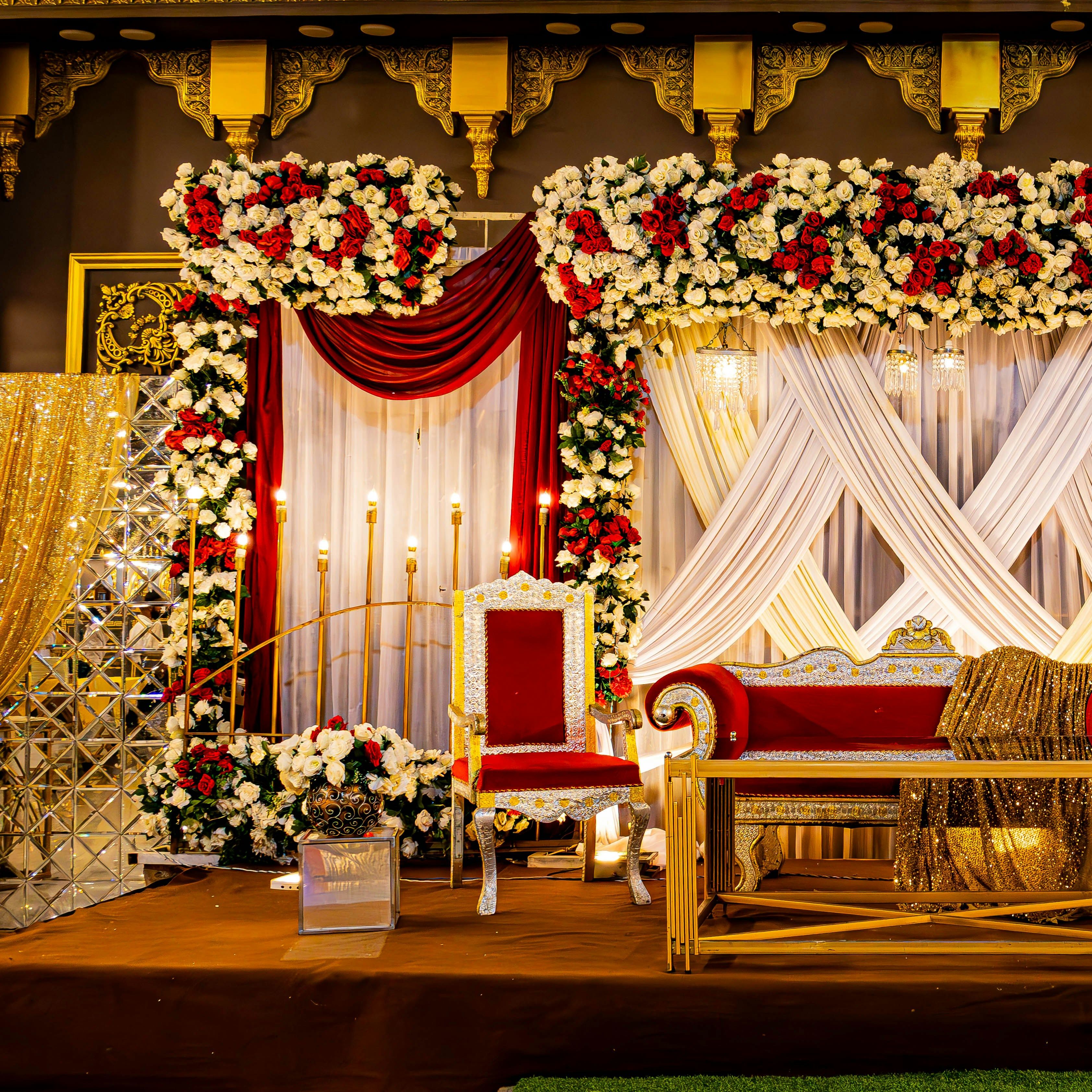 Luxurious wedding stage decorated with red and white flowers, ornate chairs, and gold accents