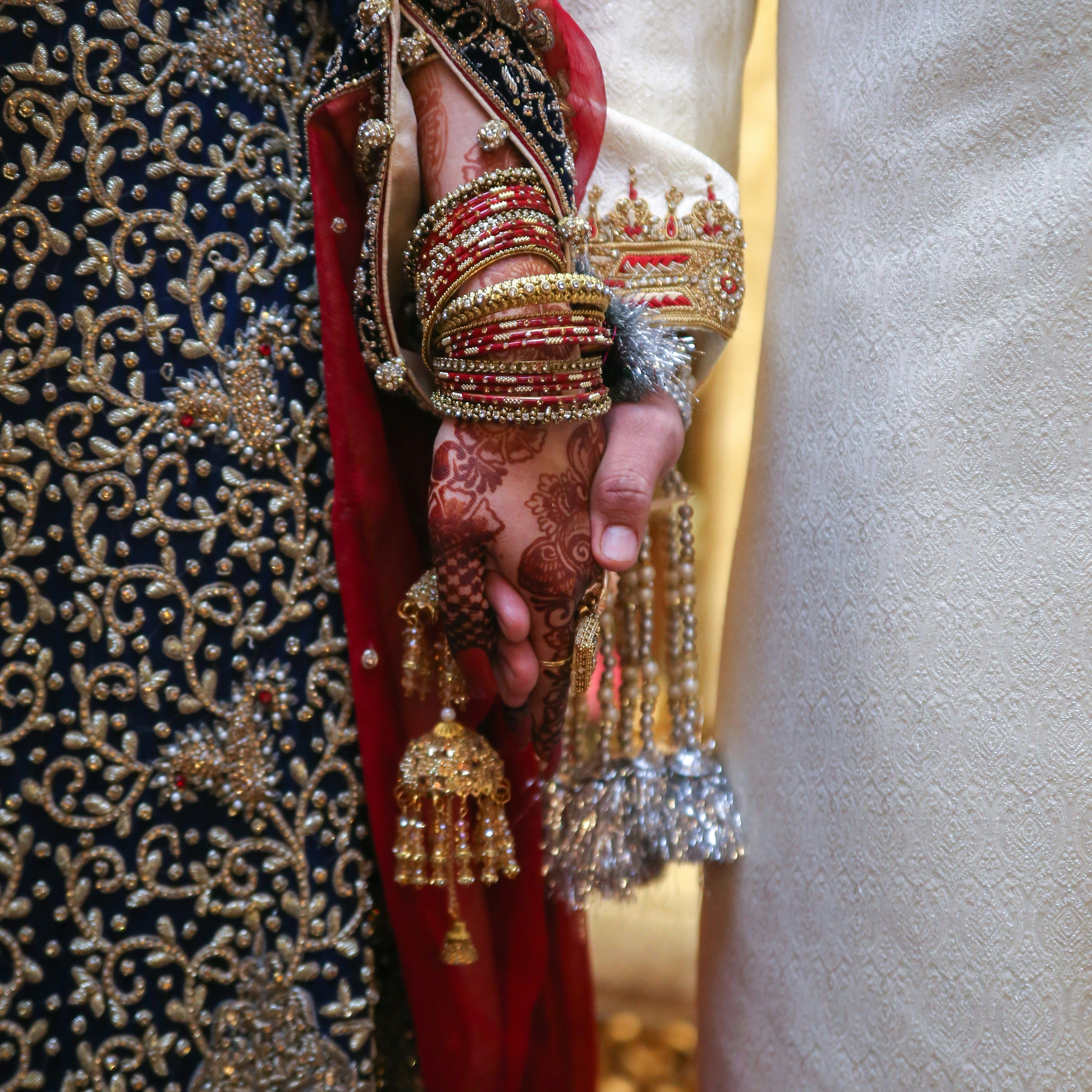 Close-up of a bride and groom holding hands in traditional South Asian wedding attire.