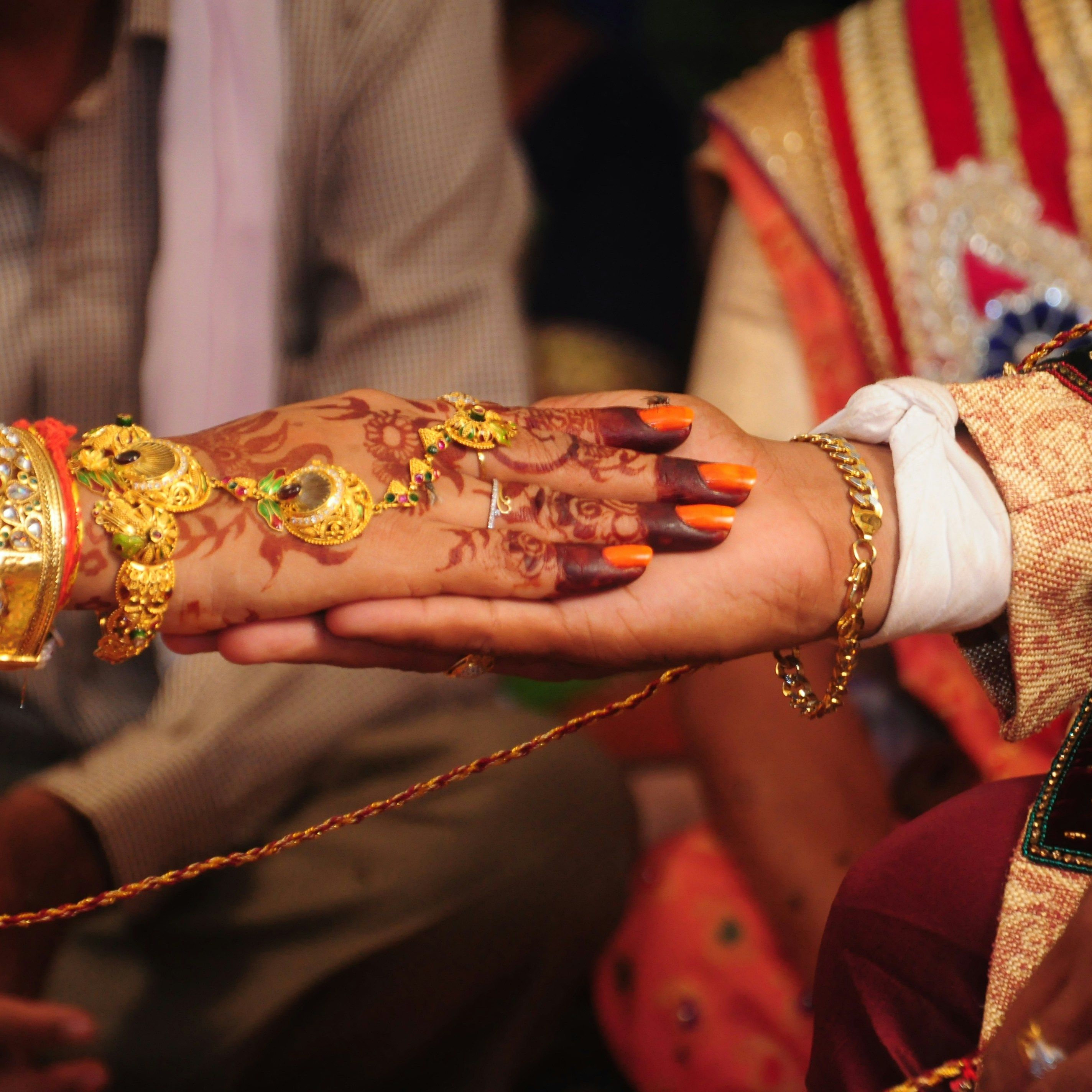 Close-up of bride and groom holding hands during Indian wedding ceremony with henna and gold jewelry visible