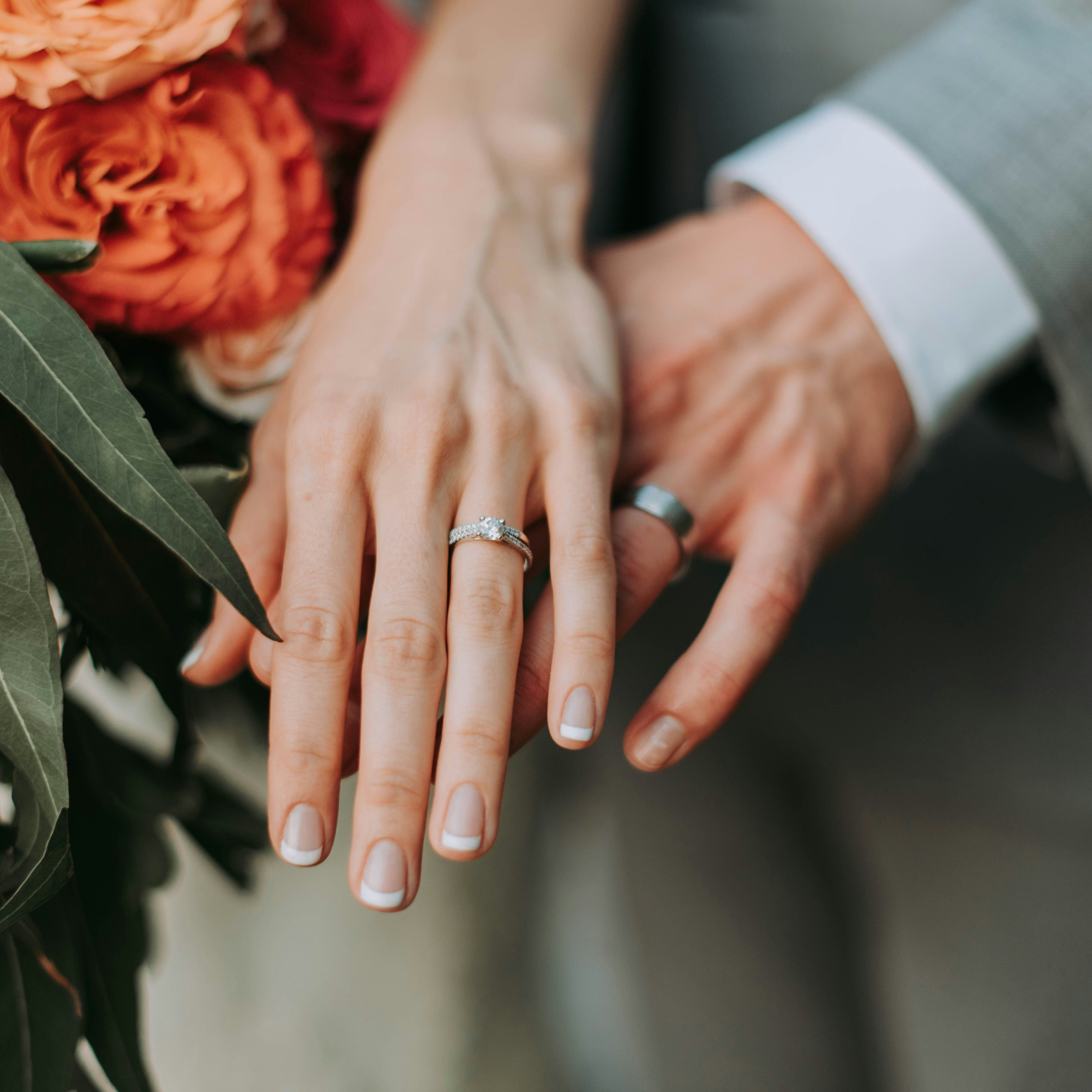 Close-up of a couple's hands with wedding rings, next to a bouquet of flowers.