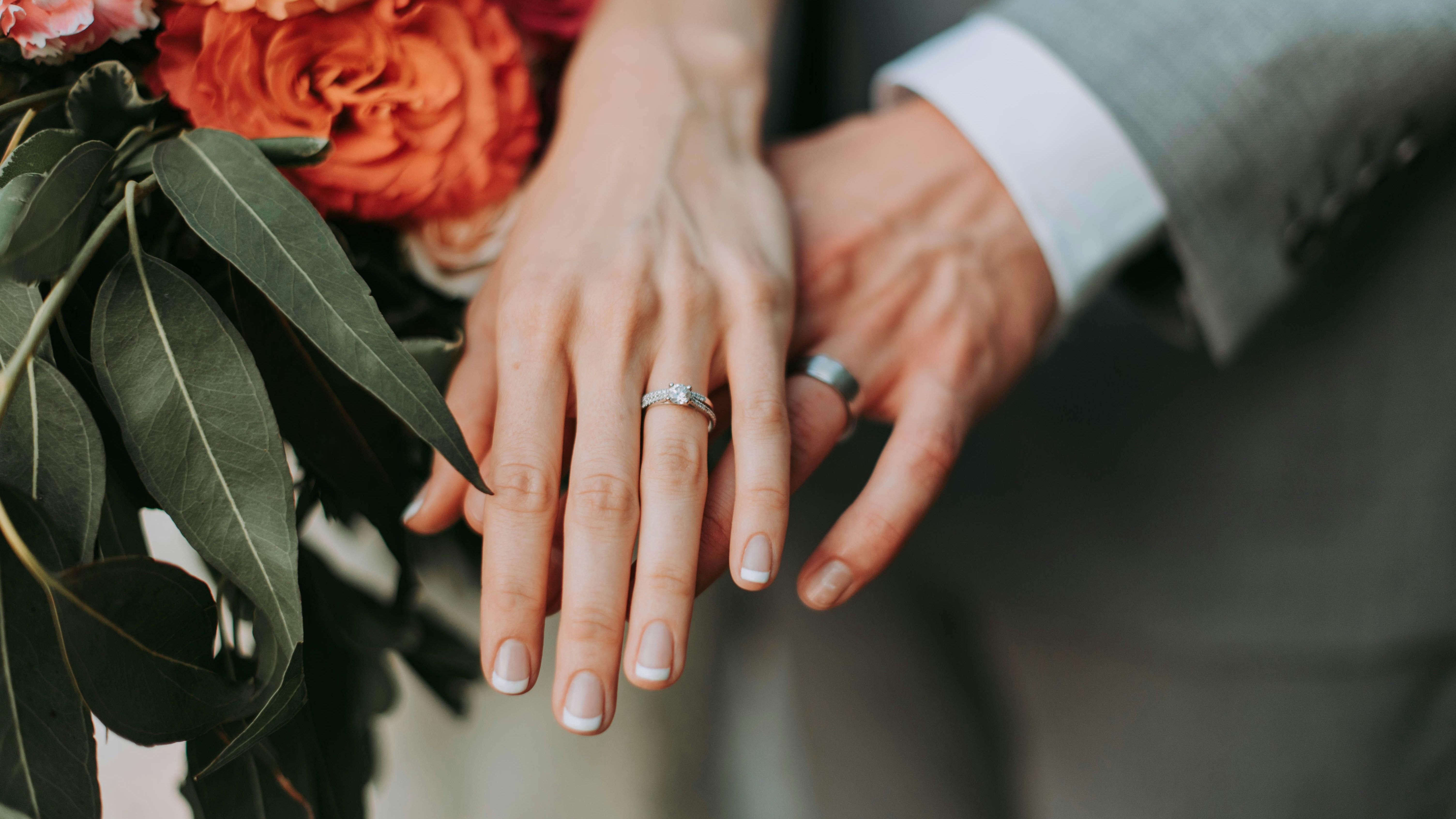 Close-up of a couple's hands with wedding rings, next to a bouquet of flowers.