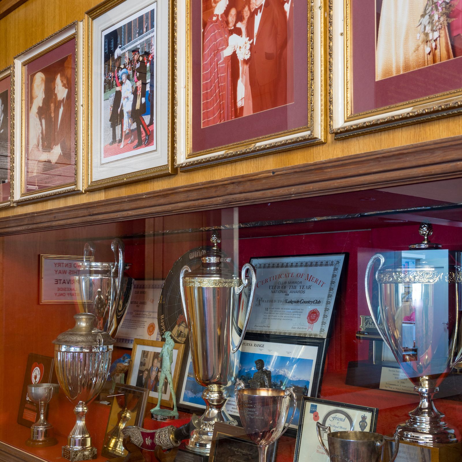 A display case containing several trophies and framed photographs on a wooden wall.
