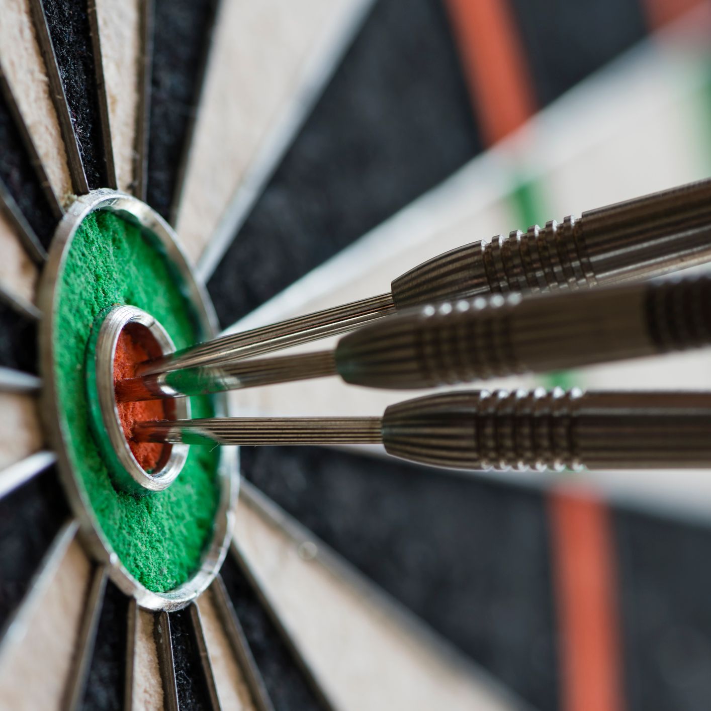 Three darts perfectly hit the bullseye on a dartboard, all clustered tightly in the red center surrounded by a green ring.