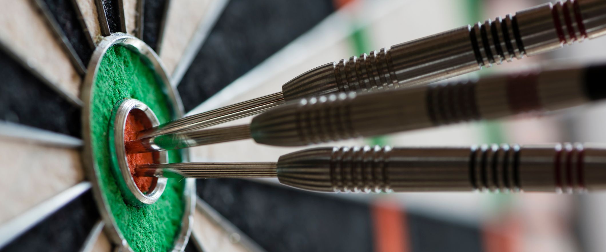 Three darts perfectly hit the bullseye on a dartboard, all clustered tightly in the red center surrounded by a green ring.
