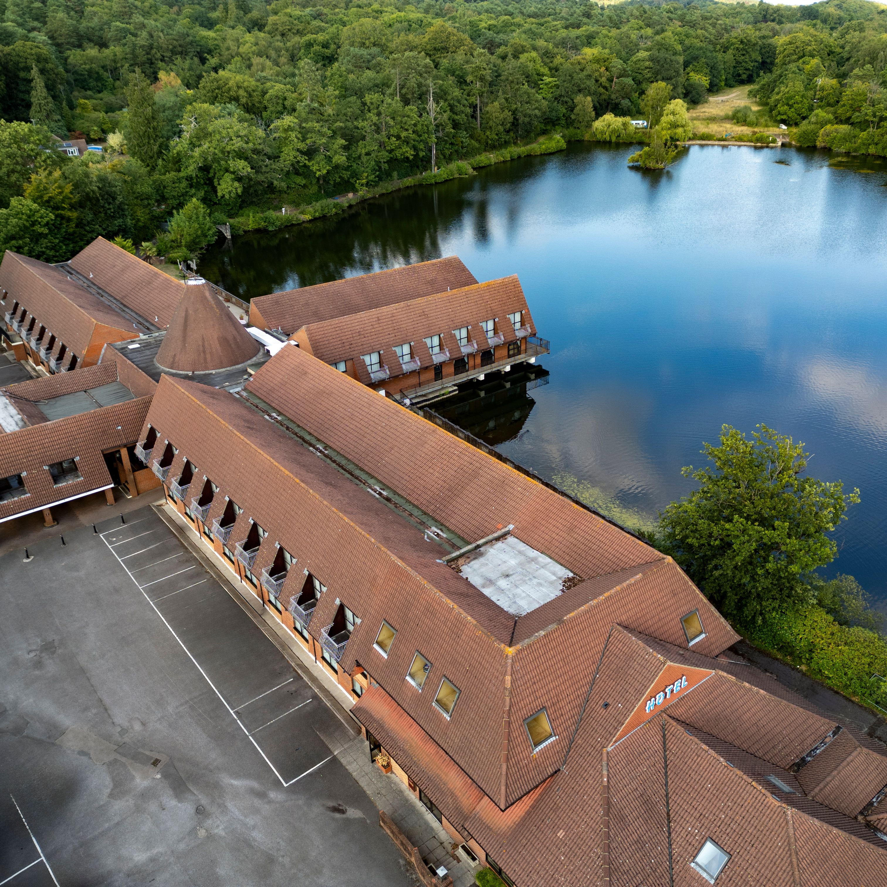 Aerial view of a hotel building situated next to a large lake surrounded by trees.