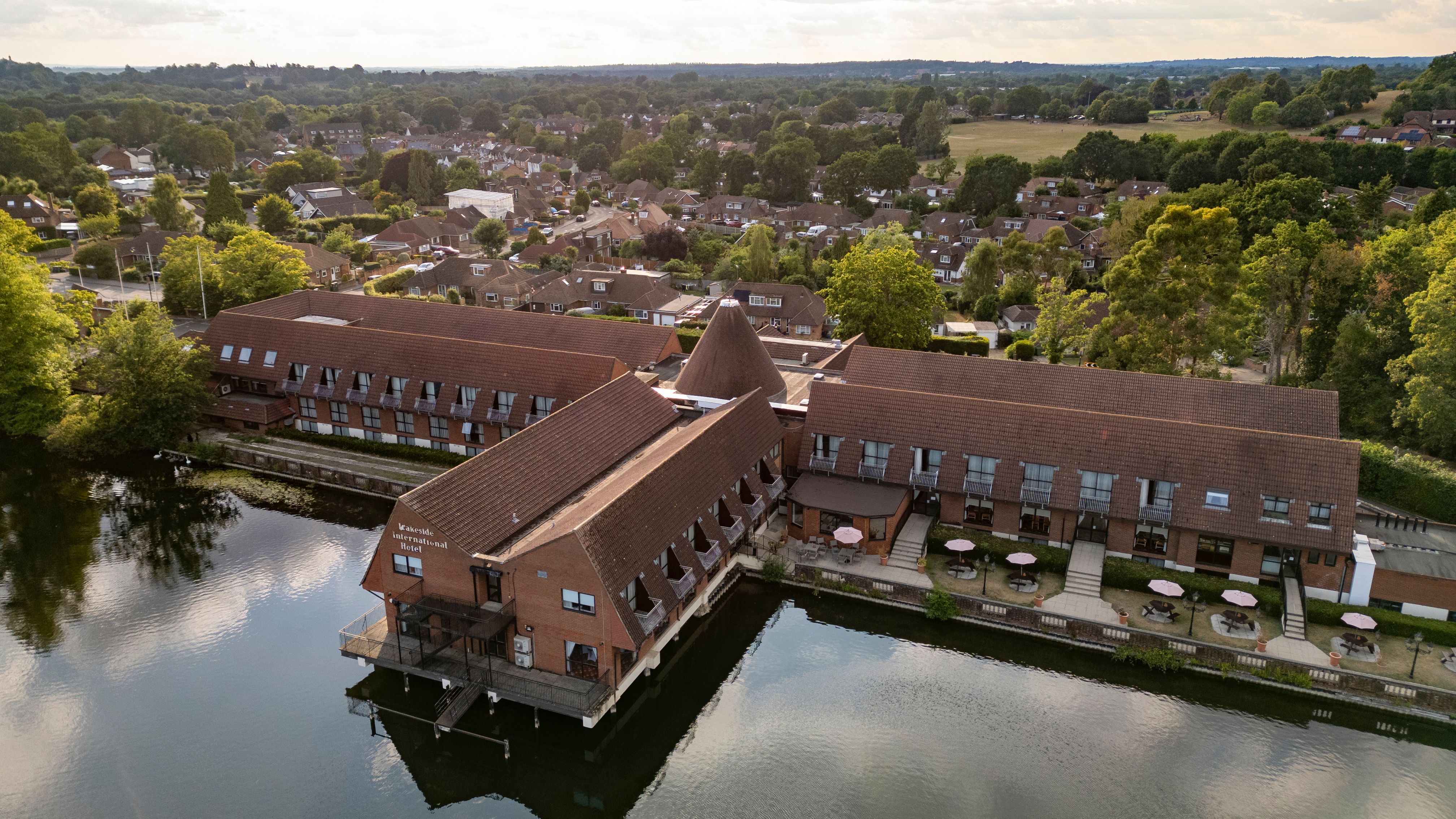 Aerial view of a large riverside hotel with red roofs surrounded by trees and residential houses.