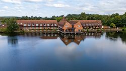 Large lakeside hotel with red roofs and brick facade reflected in calm water.