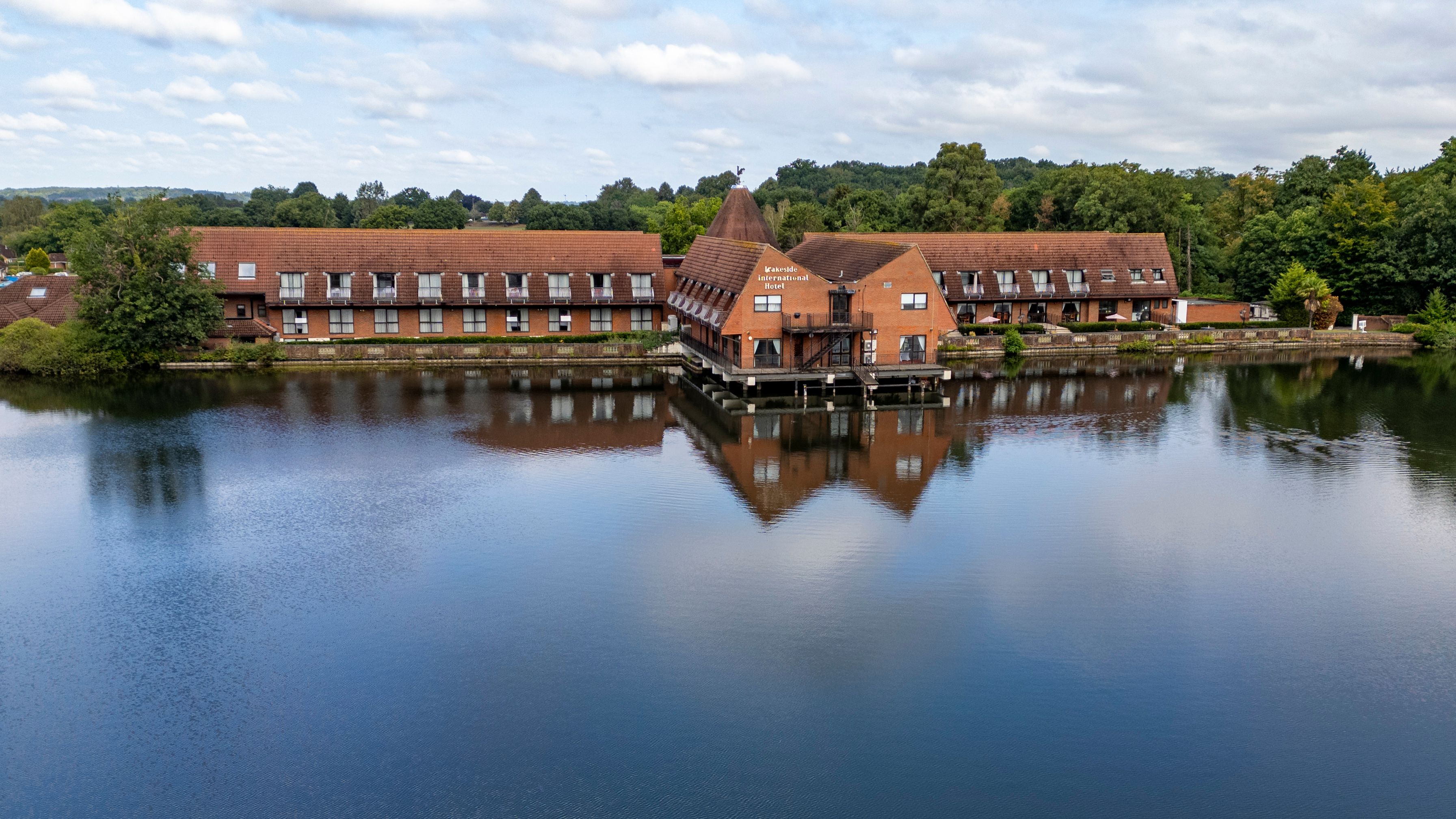 Large lakeside hotel with red roofs and brick facade reflected in calm water.