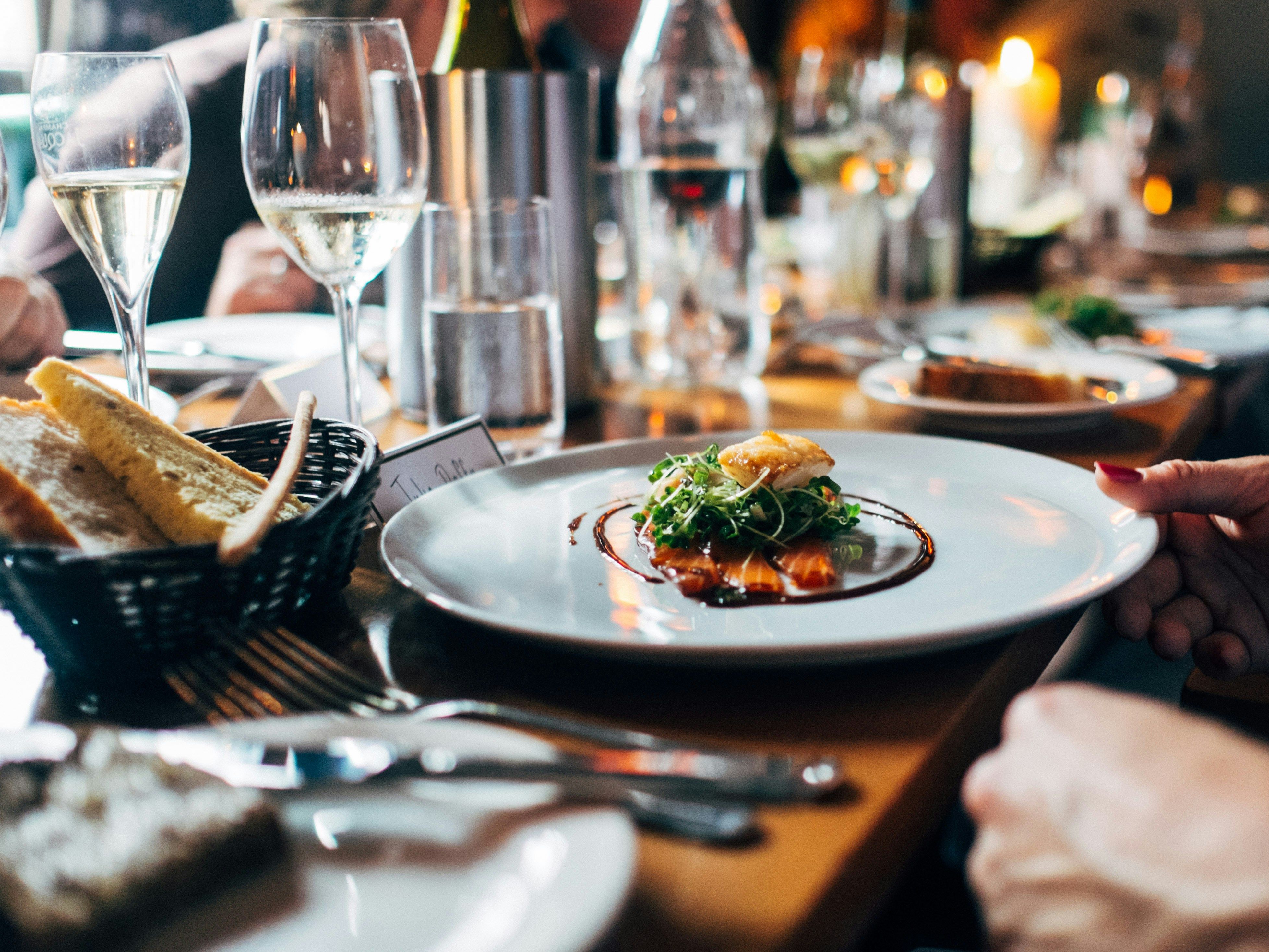 Elegant restaurant table setting with fine dining dish, bread basket, and glasses of white wine.