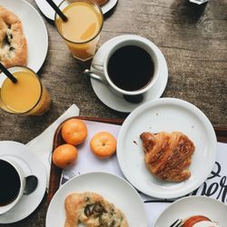 Breakfast table with coffee, orange juice, pastries, tangerines, and a dessert.