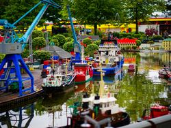 Miniature harbor scene built from LEGO bricks with ships, cranes, and buildings beside a waterway.