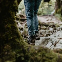 Person wearing jeans and hiking boots standing on a rocky trail in a forest