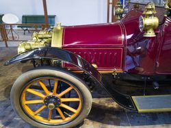 Close-up of a vintage red car with brass details and wooden-spoked wheels